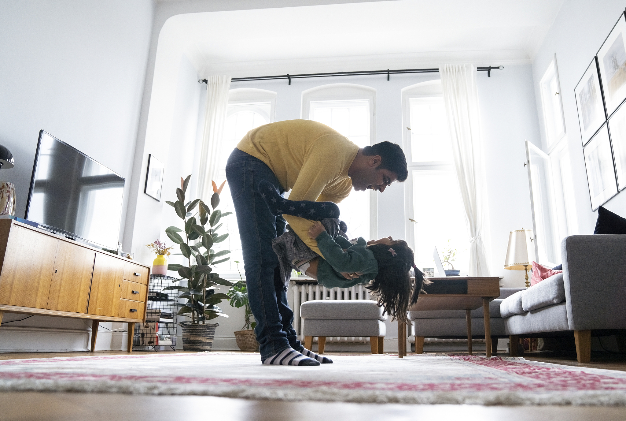 playful man carrying daughter in living room