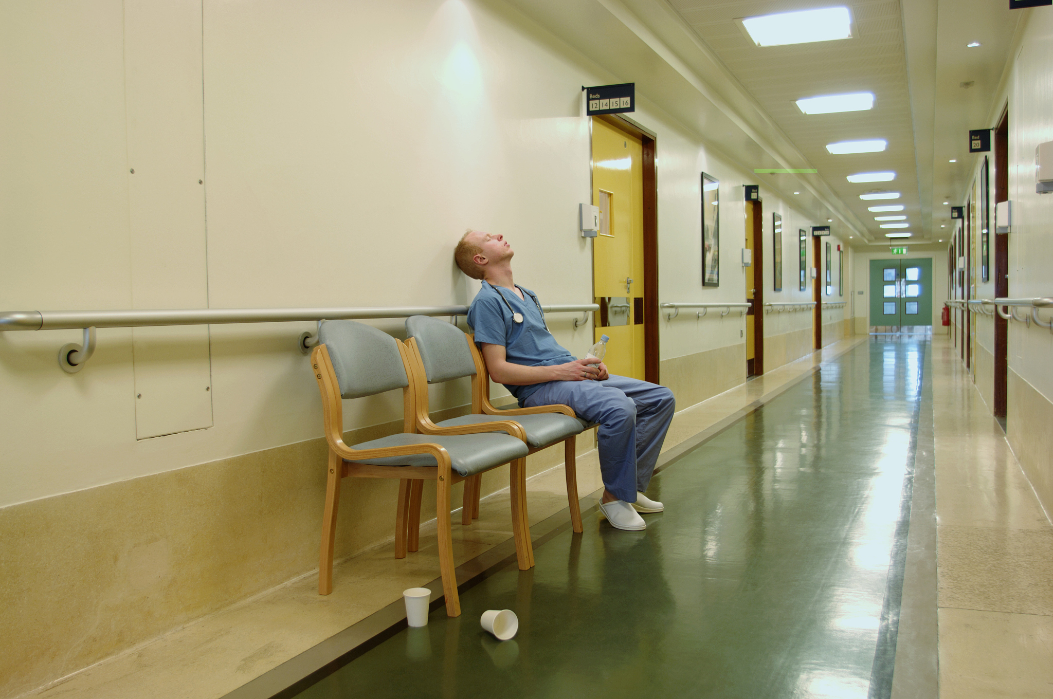 young male doctor on chair in corridor, head against wall, eyes 