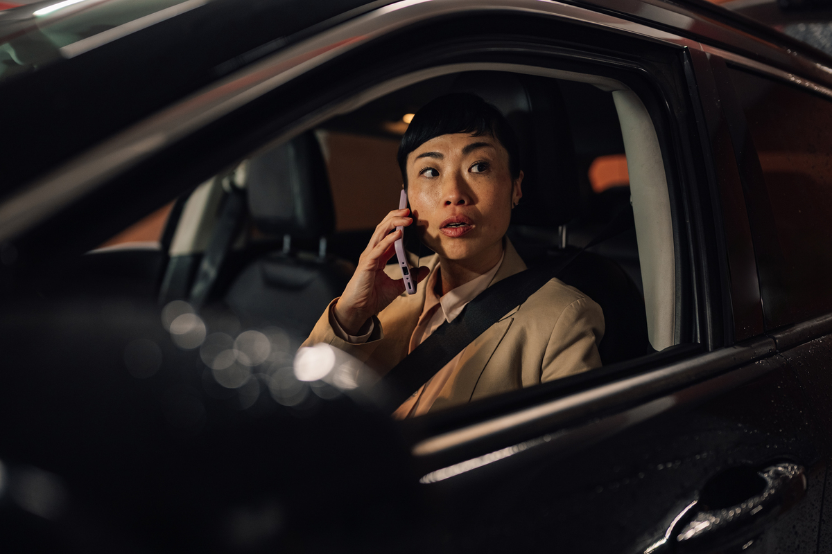 夜间,女子在车内认真地与人通话,她在开车,体现城市的
