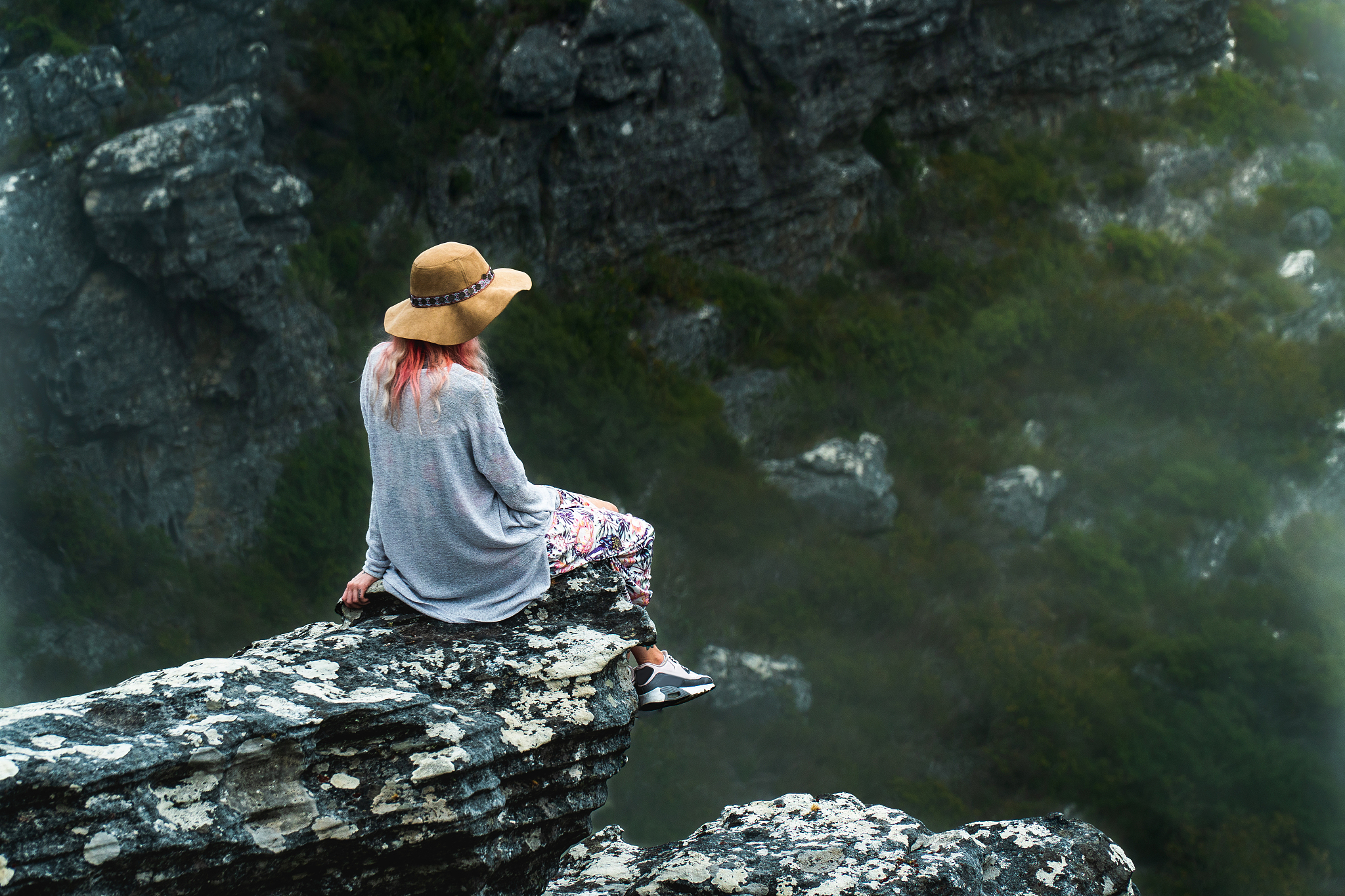 woman sat on cliff edge surrounded by clouds