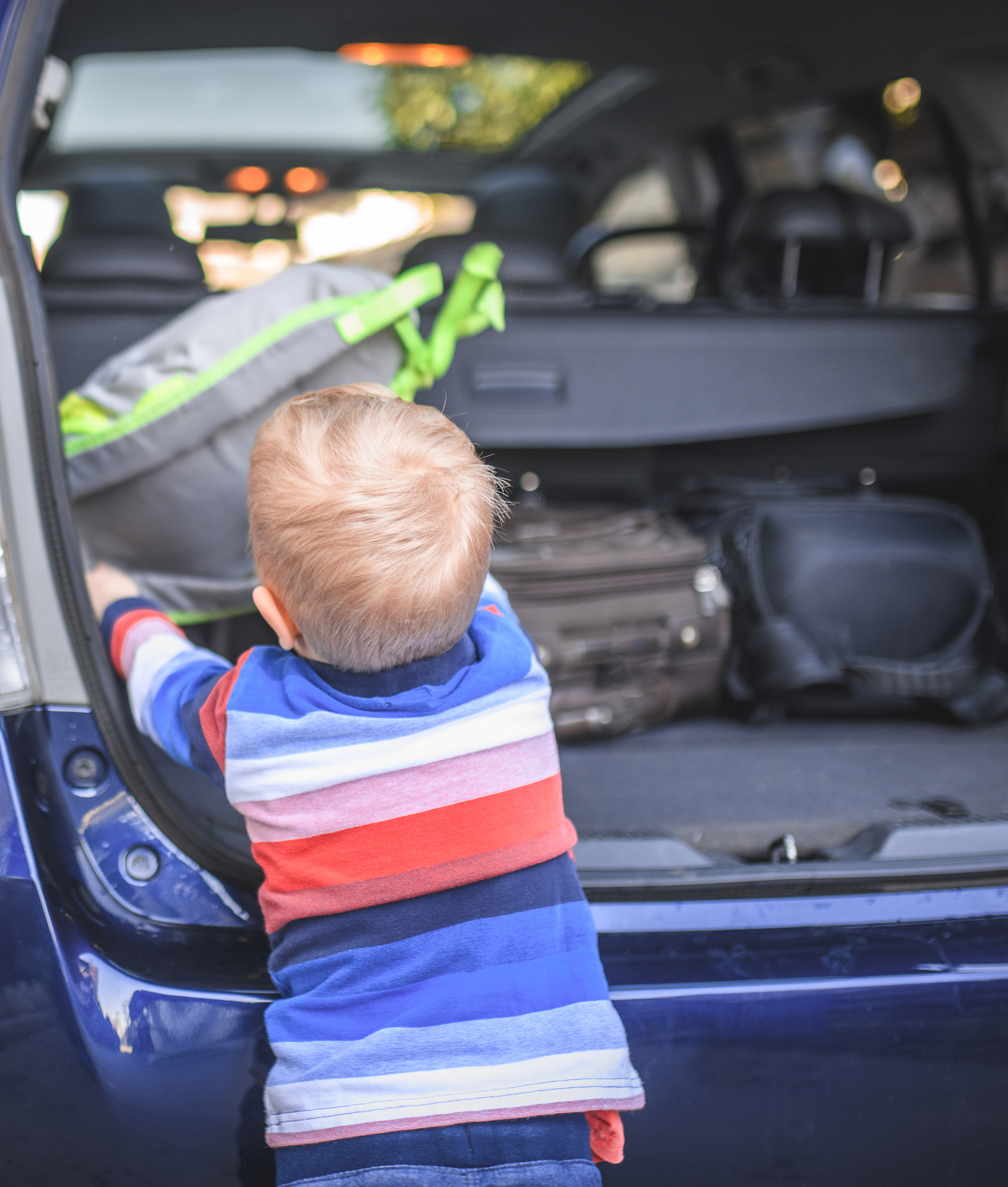 young boy packing backpack into a car trunk