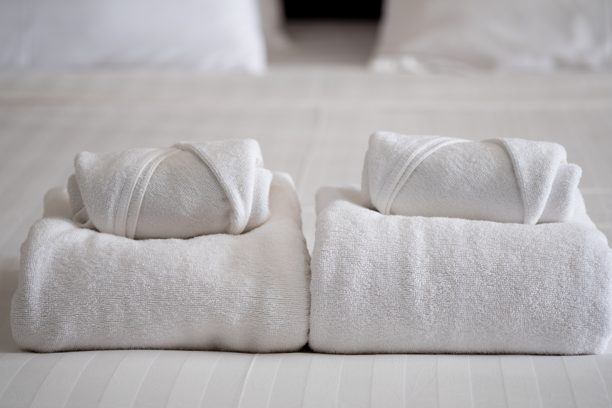 stack of white bath towels on bed sheet in modern hotel bedroom 
