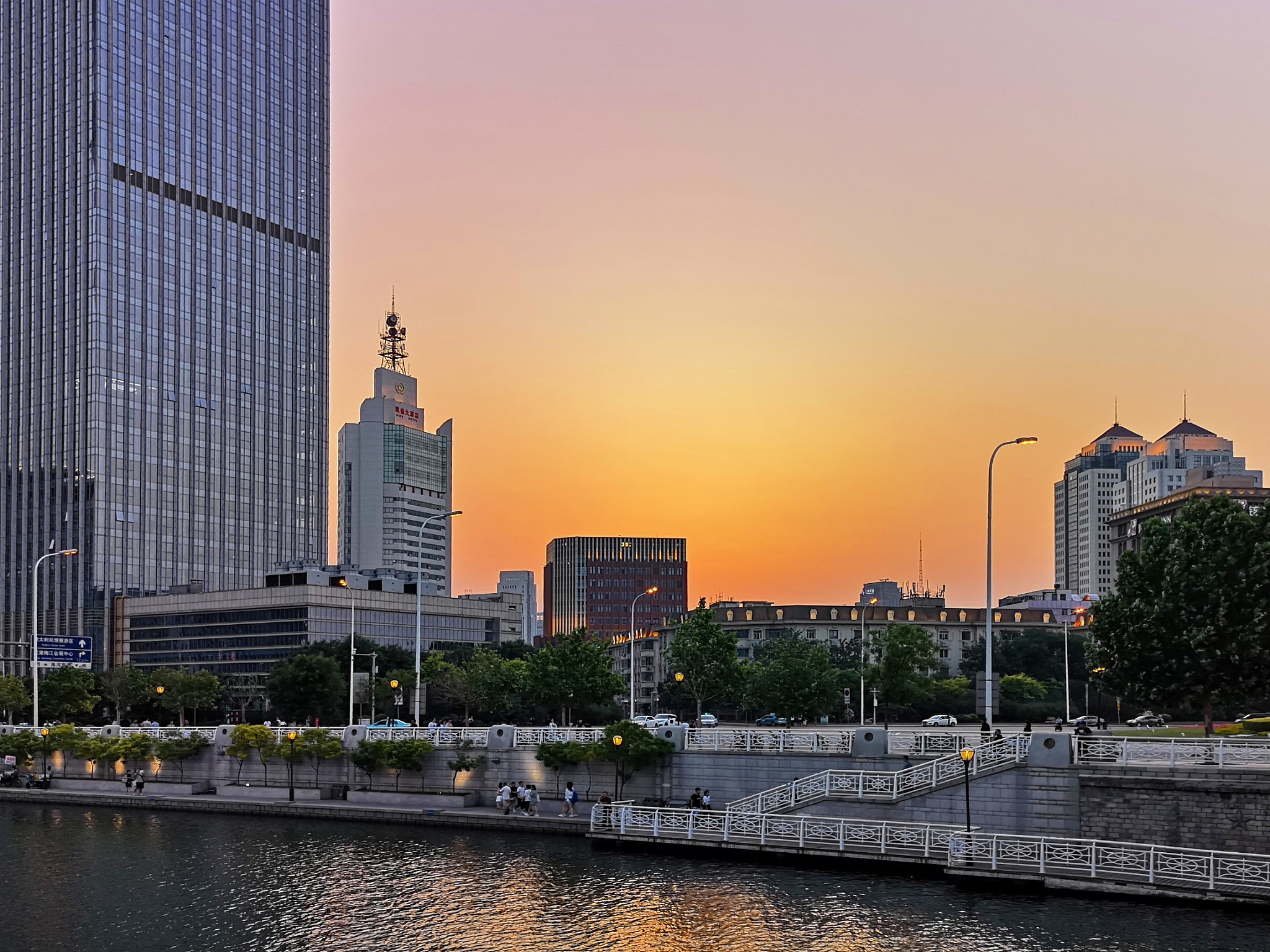 modern buildings by river against sky during sunset in city