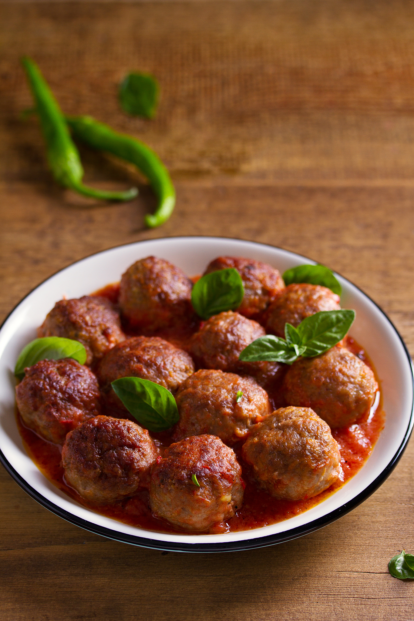 meatballs in tomato sauce, garnished with basil in bowl on woode