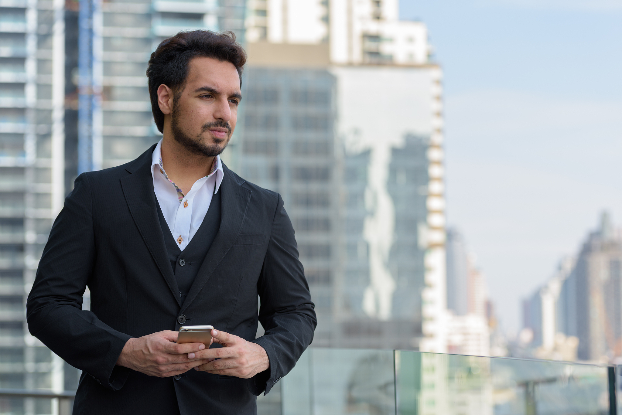 young handsome indian businessman holding mobile phone while thi