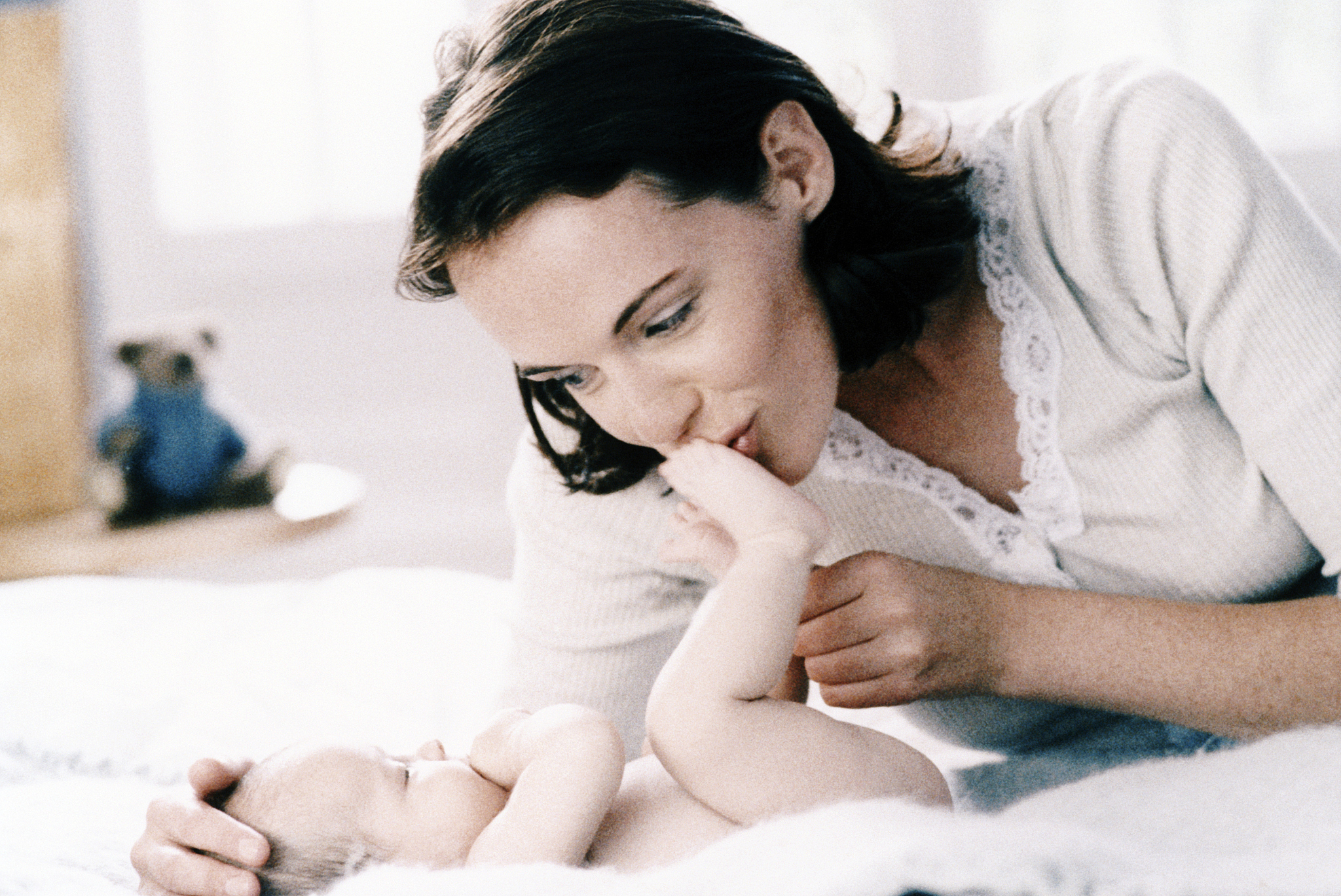 mother kissing three month babys foot on bed
