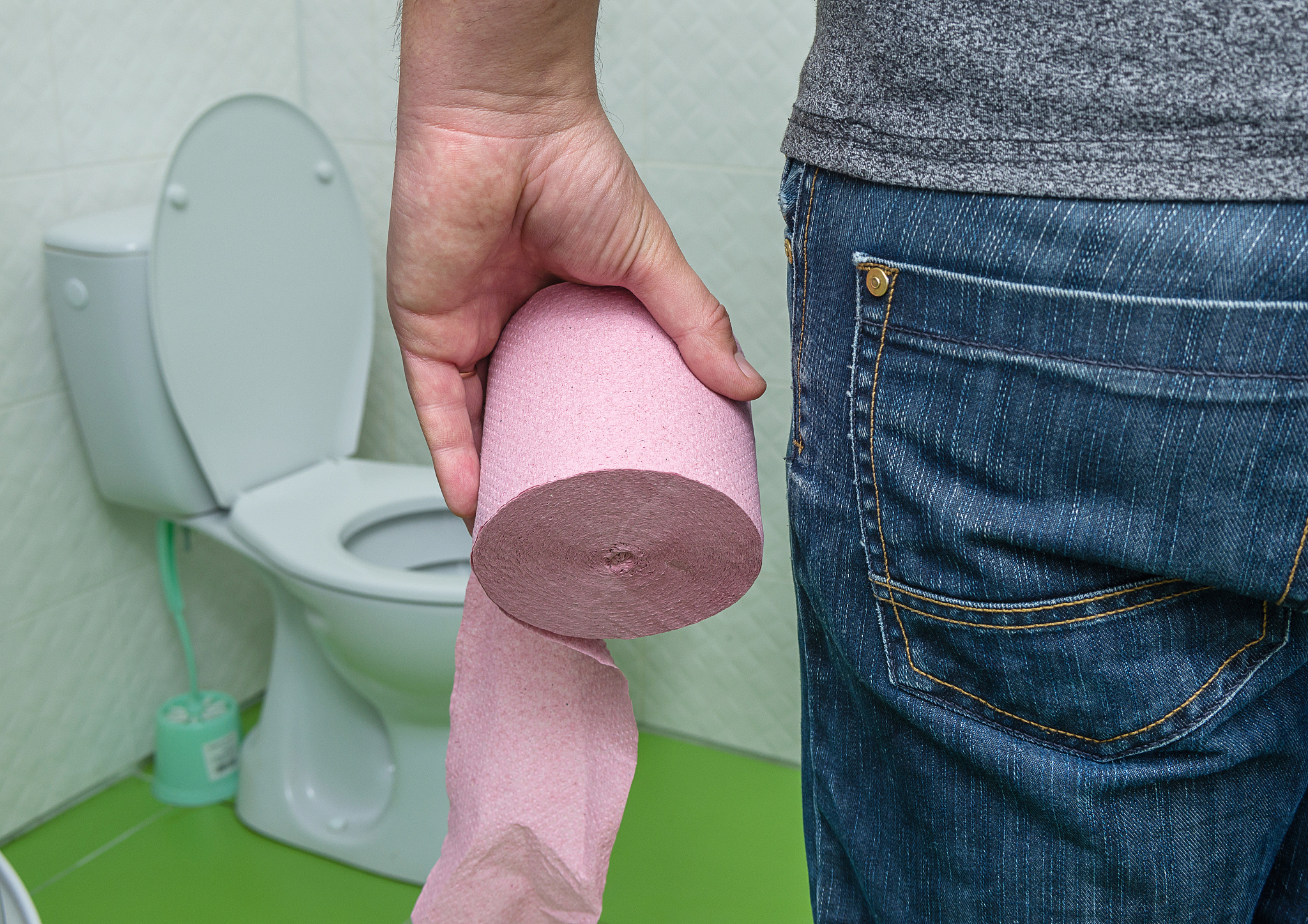 a roll of toilet paper in the hand of a man near the toilet. dia