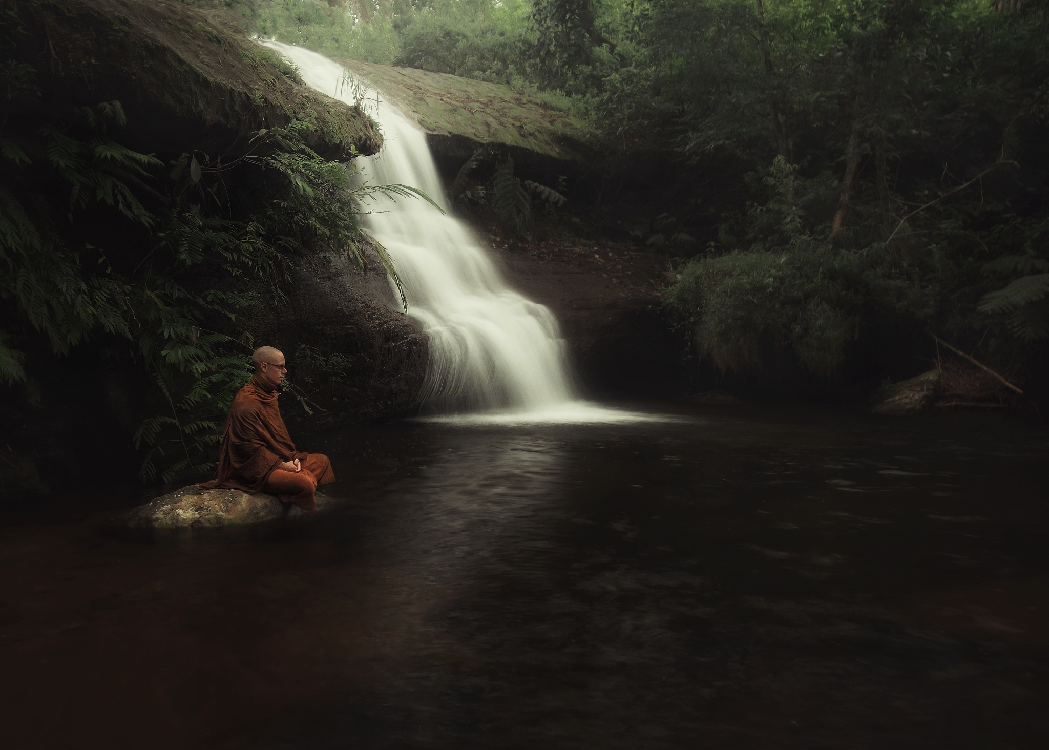 side view of monk meditating against waterfall in forest