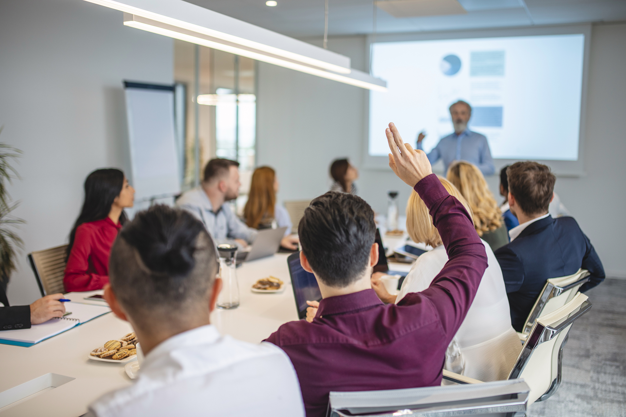 young businessman in meeting with hand raised
