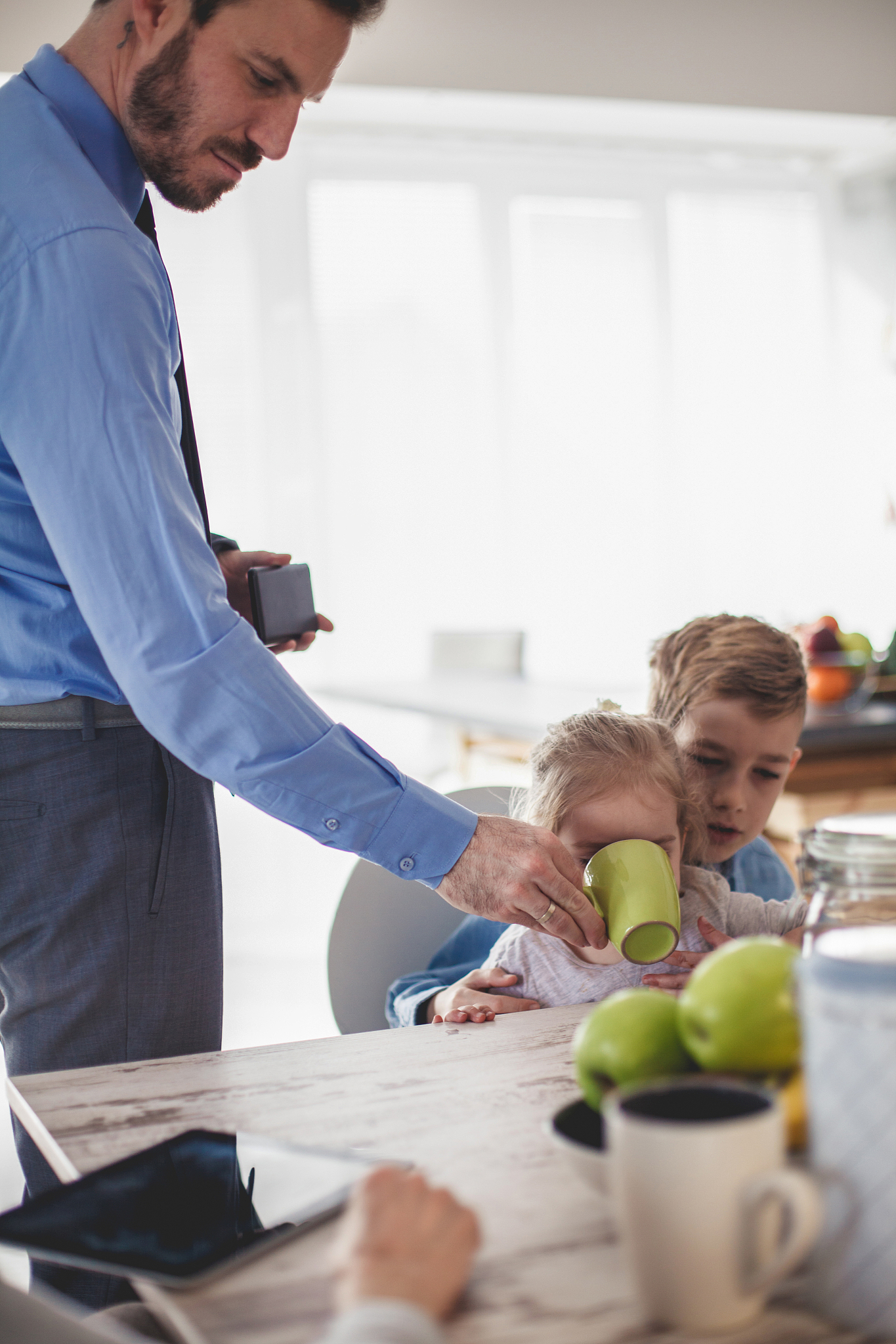 father helping his little daughter drink her tea at breakfast