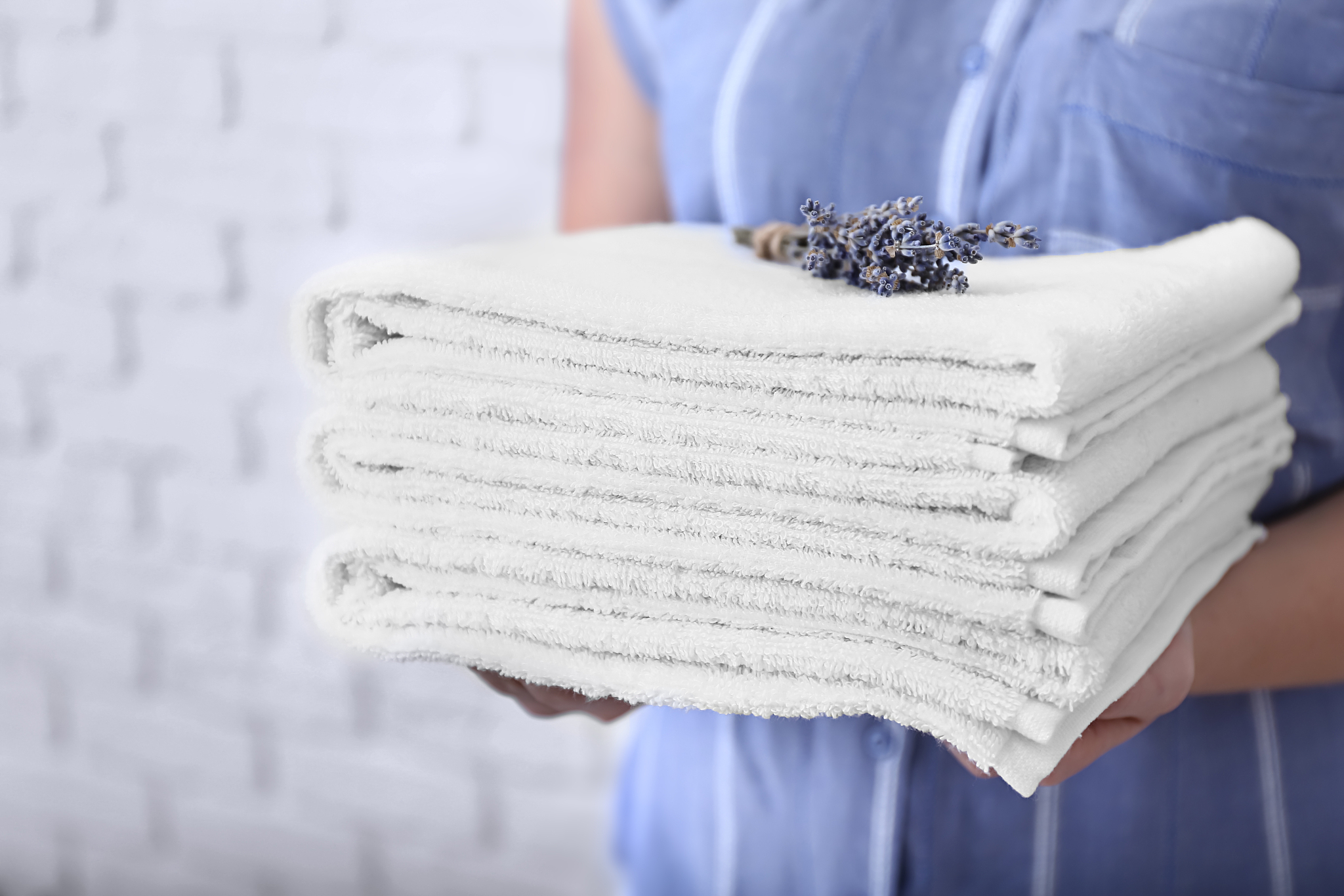 woman with stack of clean towels on light background, closeup