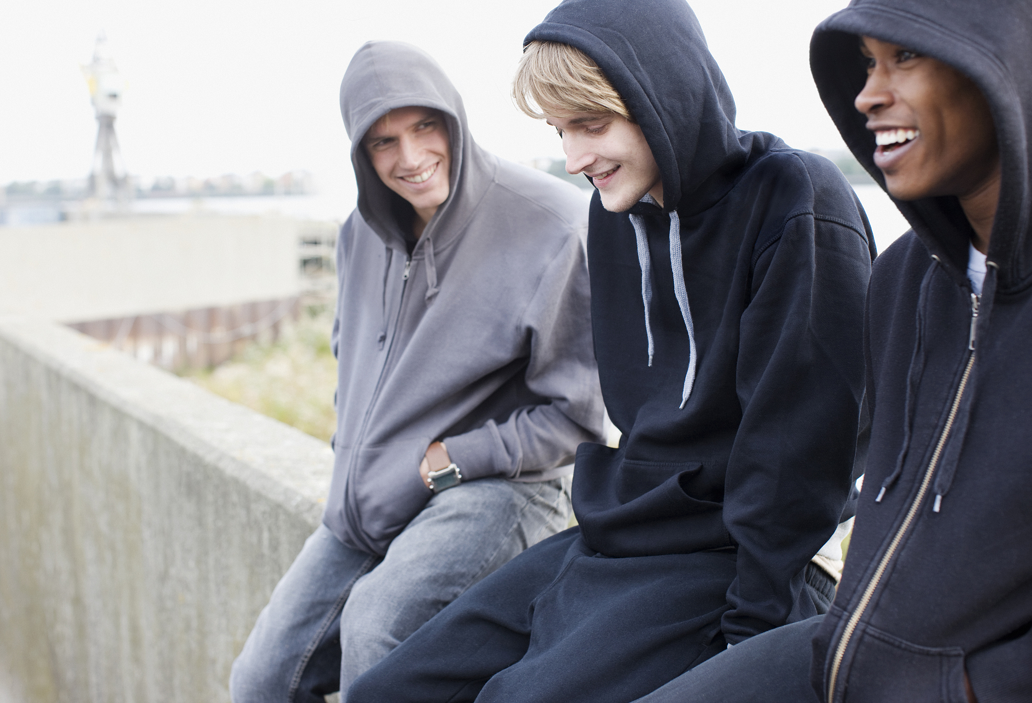 three young men in hoodies sitting on wall