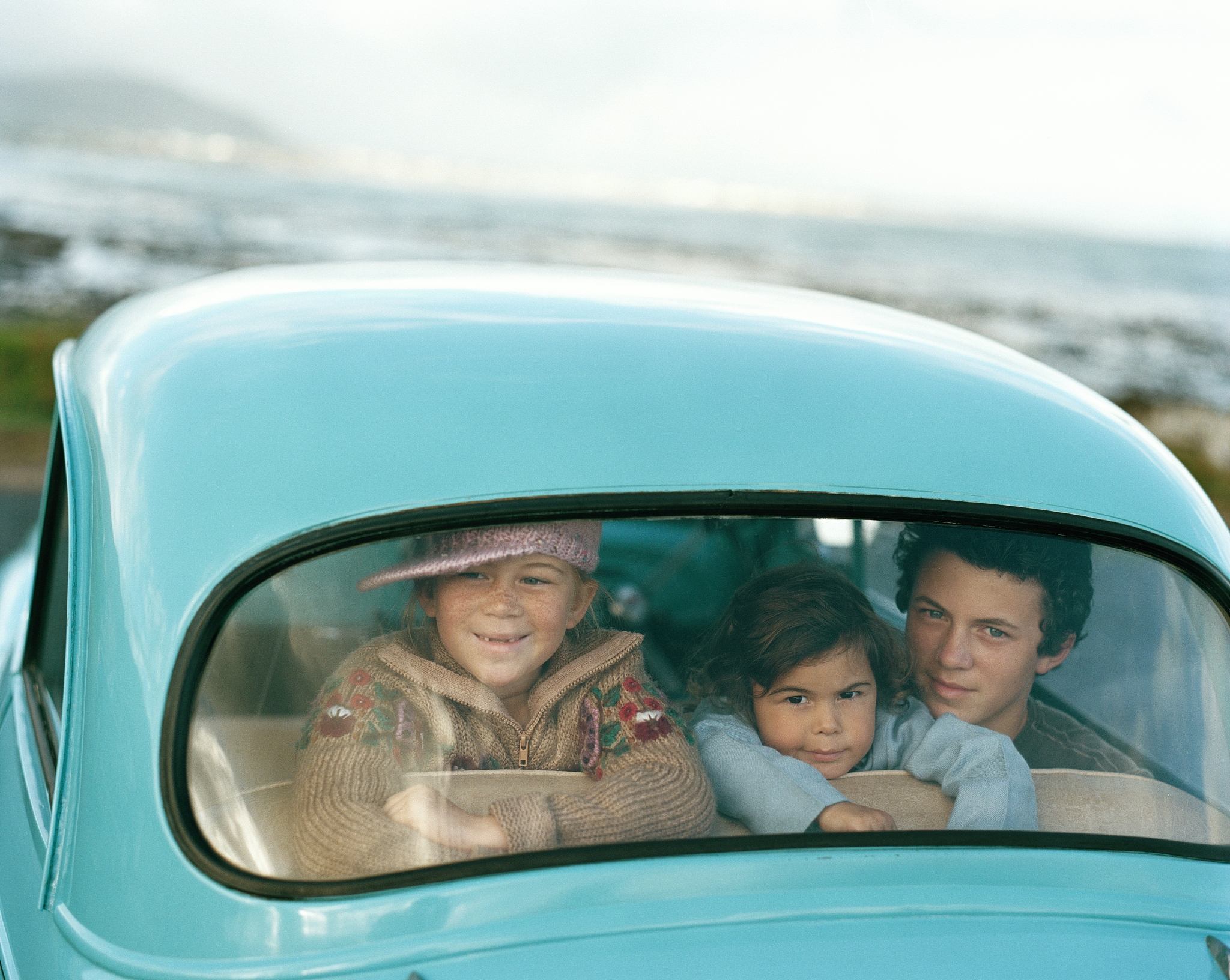 three children (3-13) in car looking through rear windscreen, po