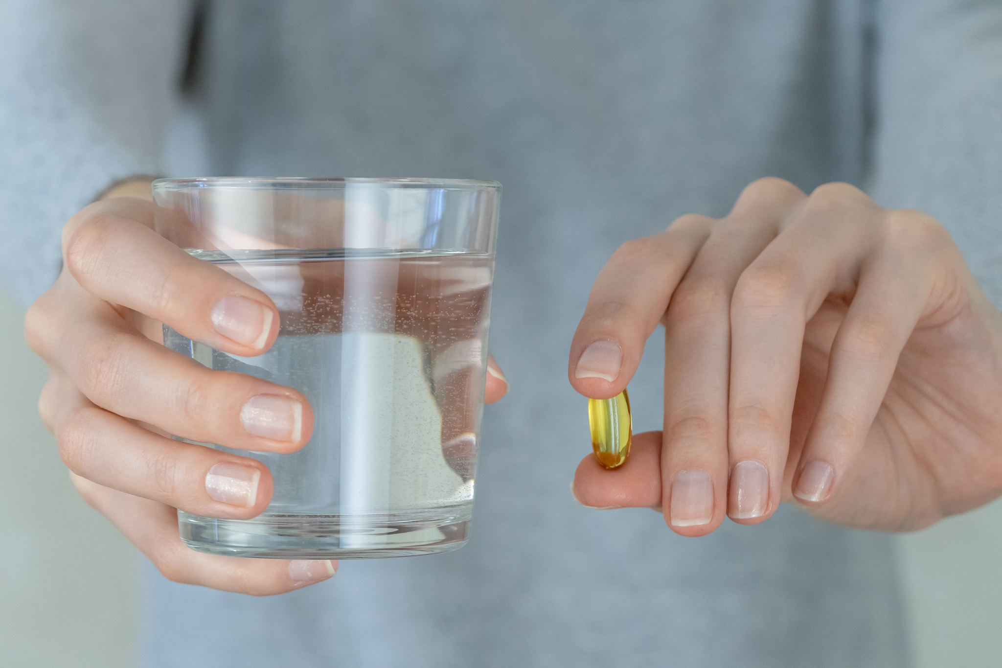 woman in a gray jacket is holding an omega-3 fish oil capsule an