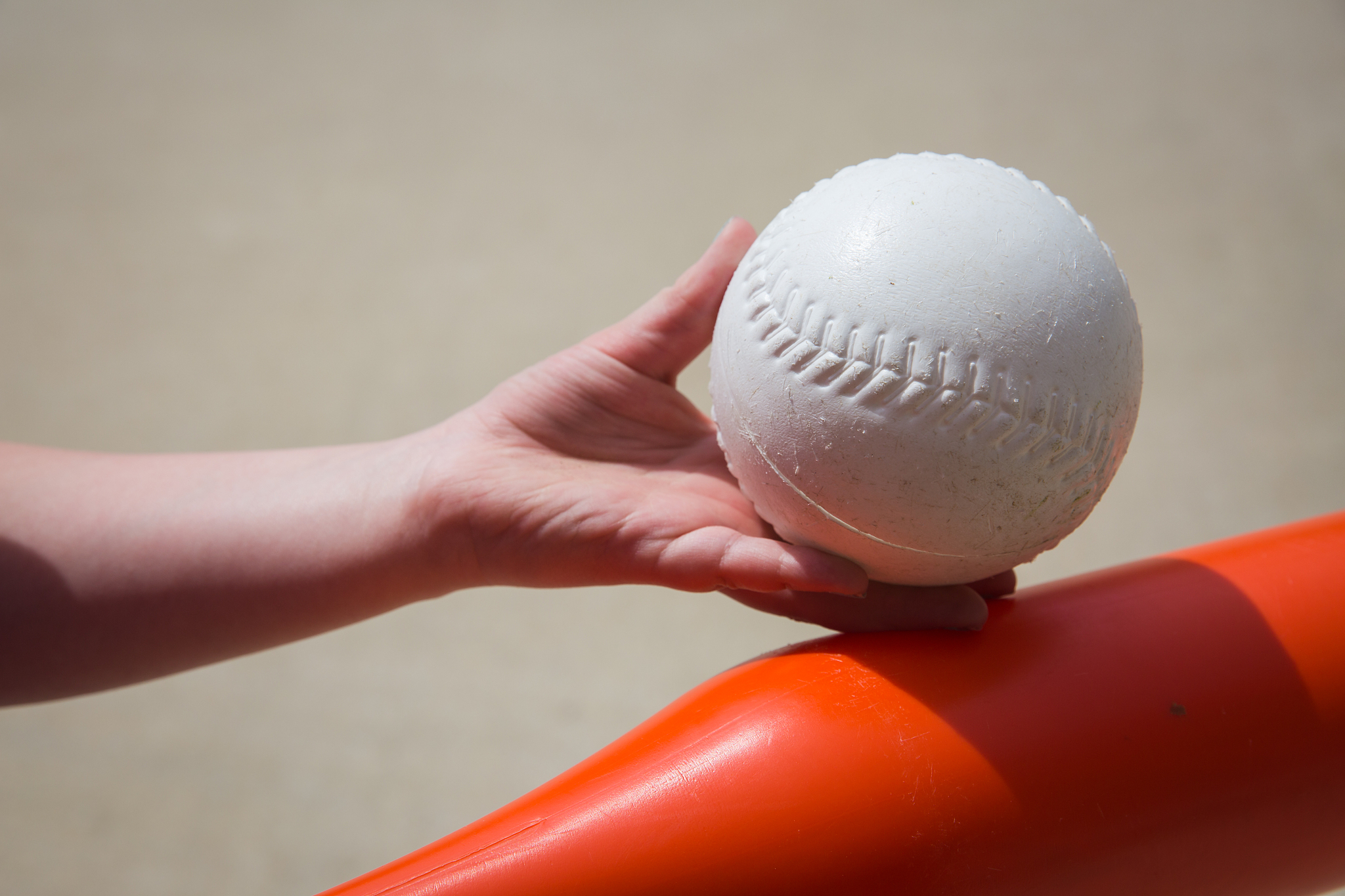 child's hand holding a white plastic baseball against a red bat