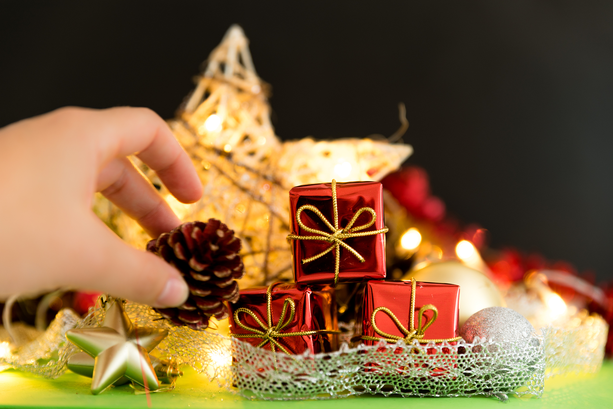 cropped hand holding pine cone by red christmas presents on tabl