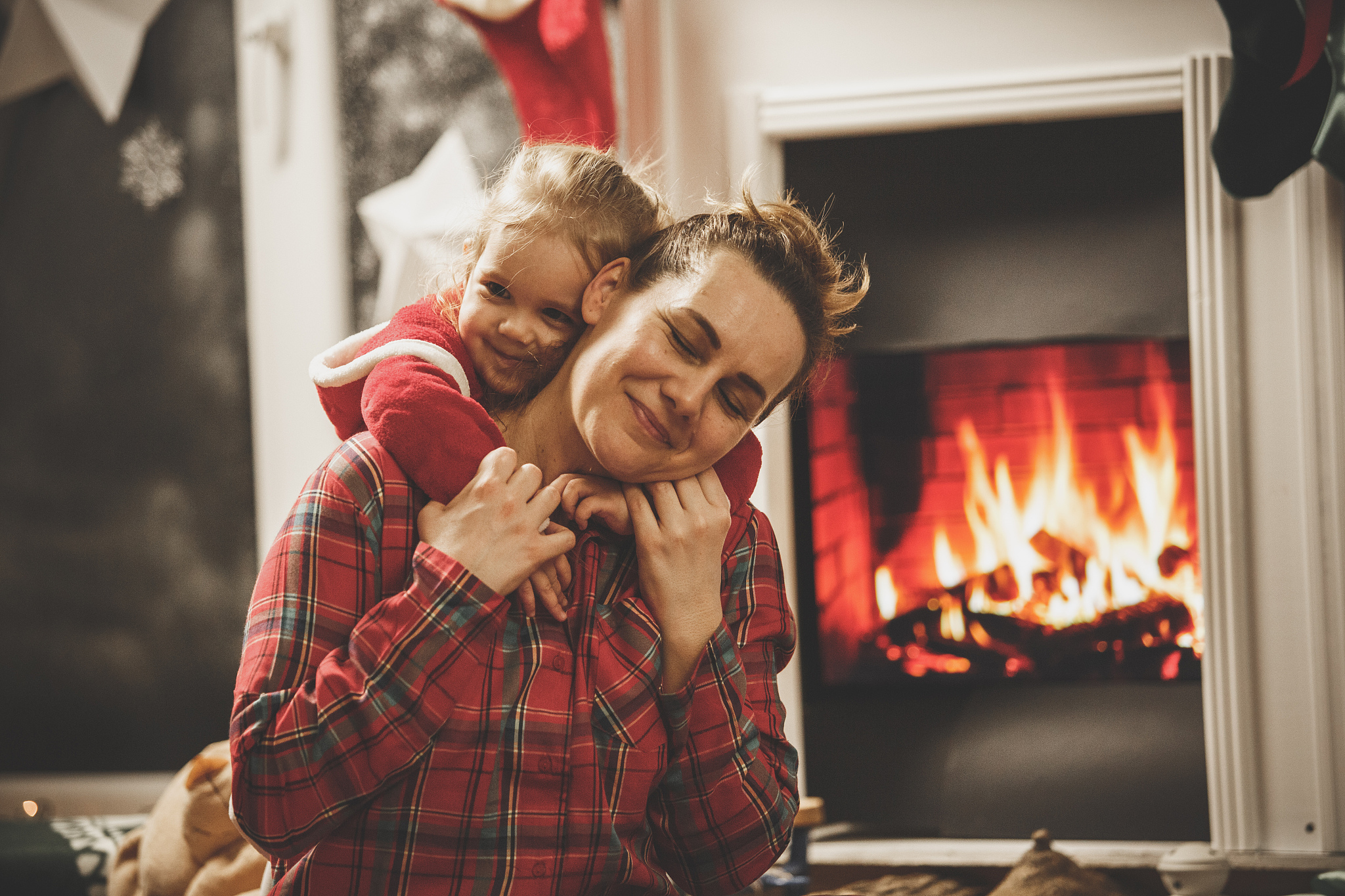 little girl hugging her mother by the fireplace