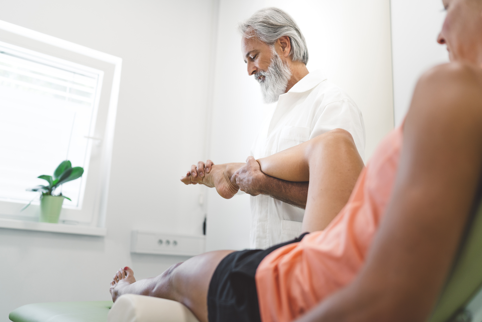 seniro bearded physical therapist massaging patient foot