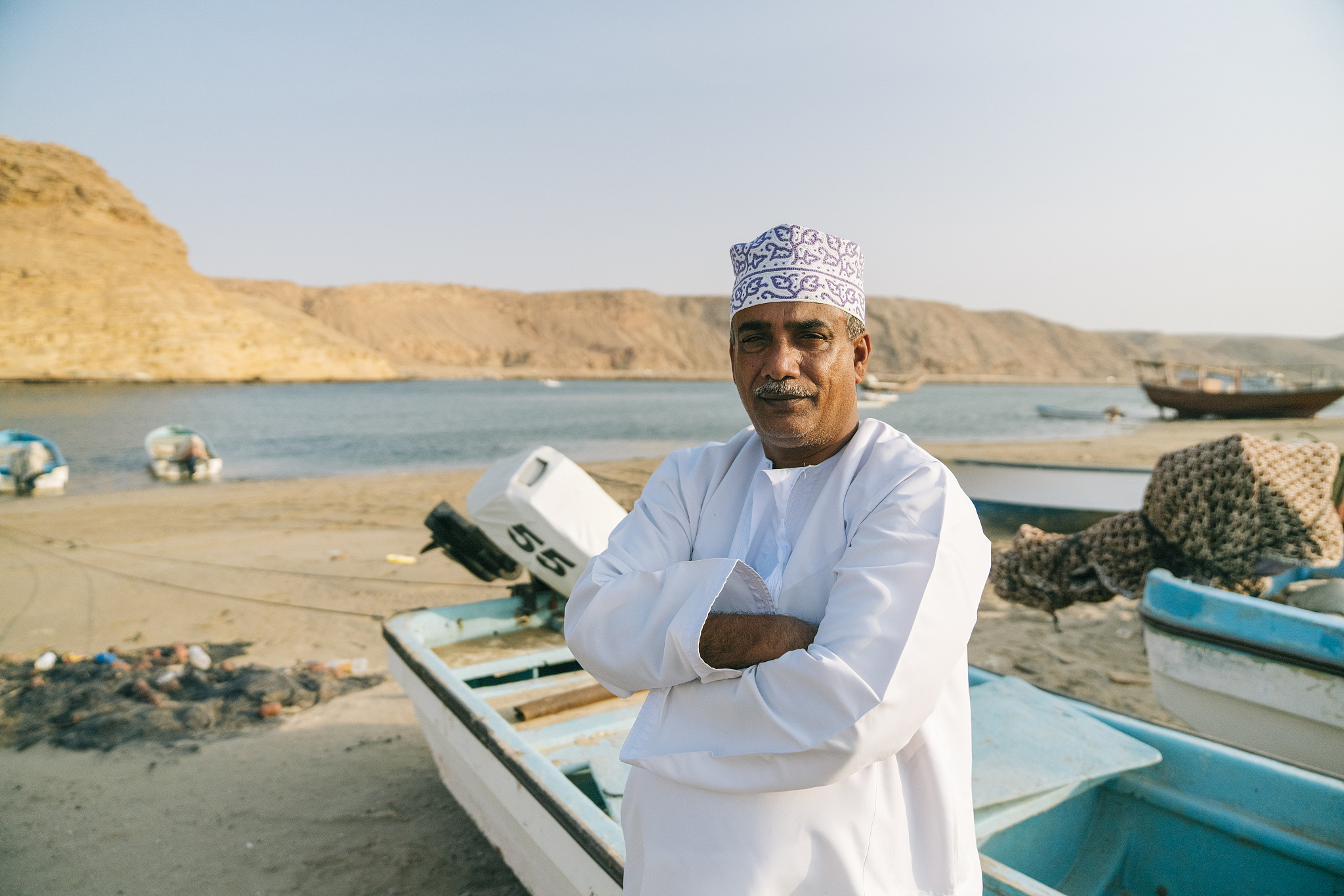 middle eastern man stands in front of small boats at port