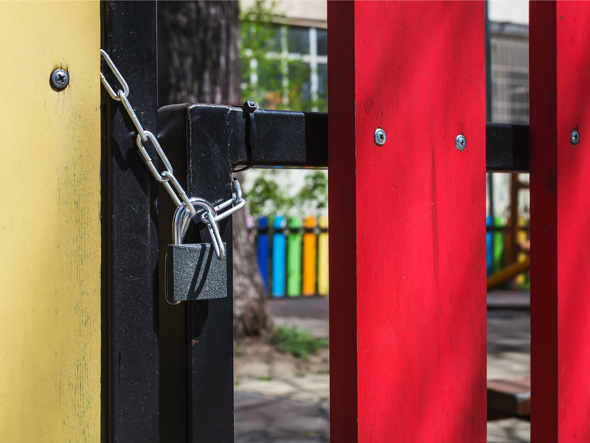 padlock locks the gate of a fenced outdoor playground on a sunny
