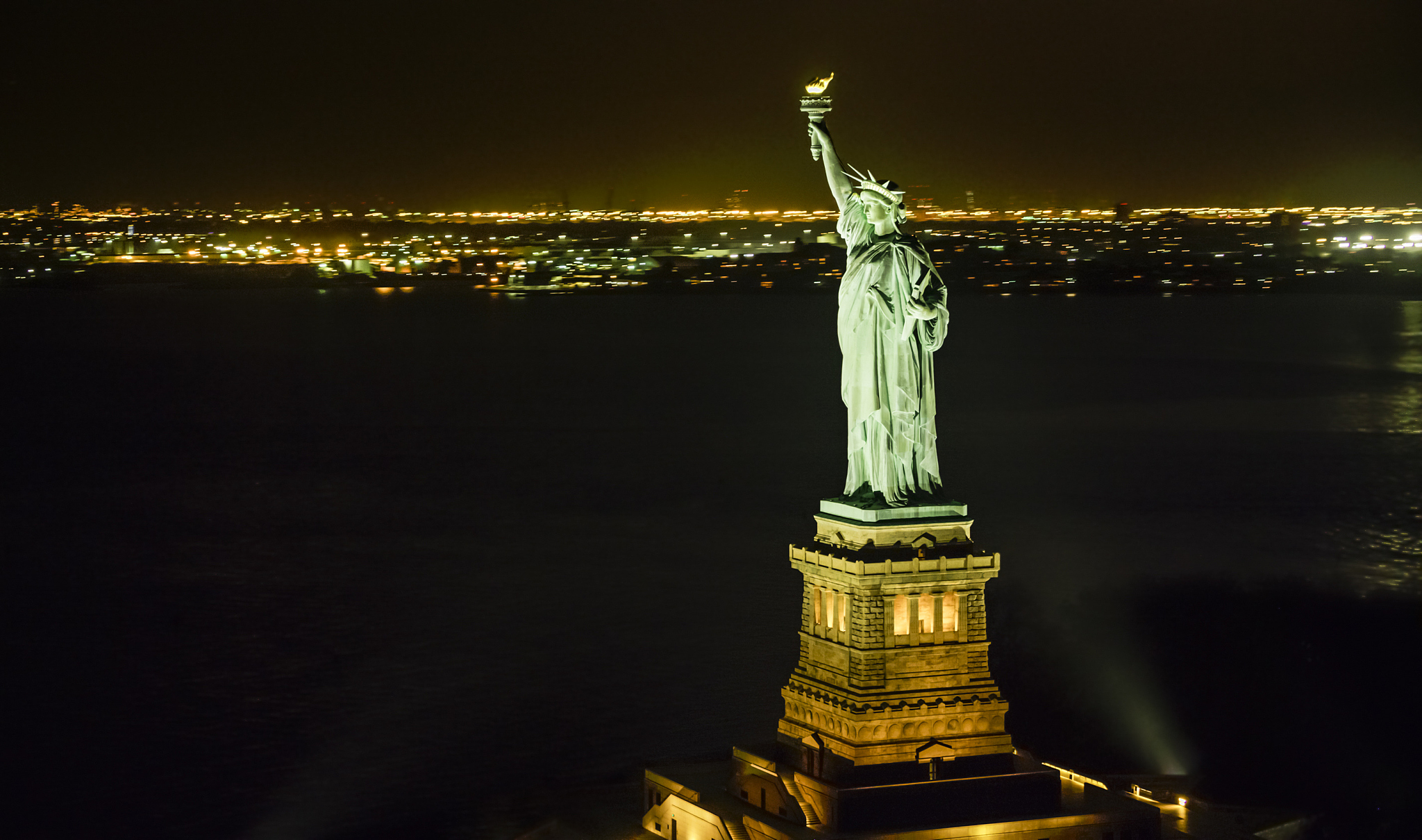 statue of liberty shining in the night with lower manhattan seen