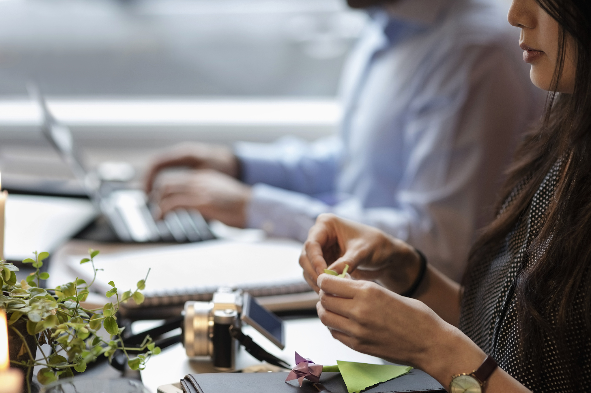 cropped image of woman making origami while sitting by coworker 
