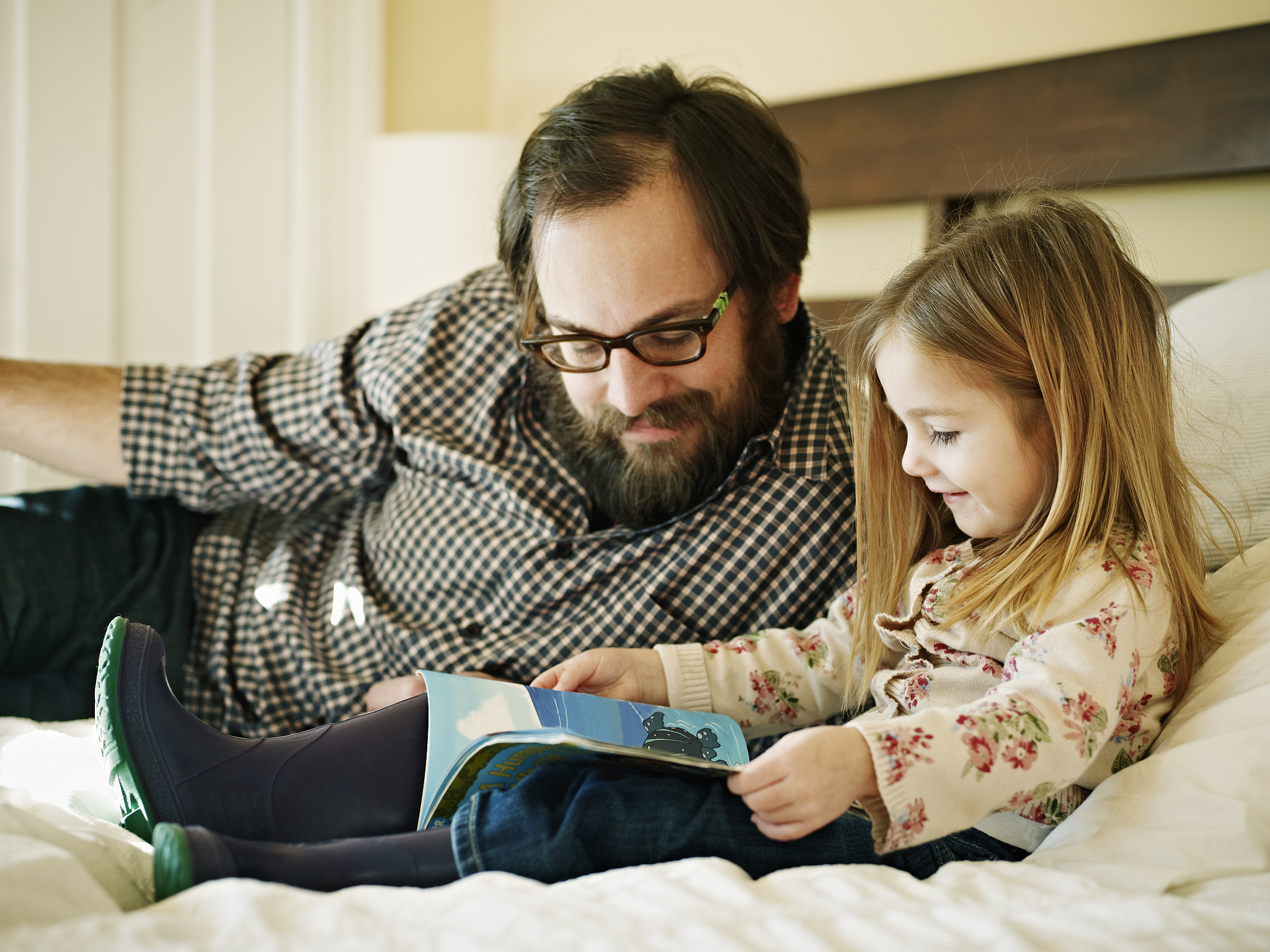 father and daughter reading book in bed