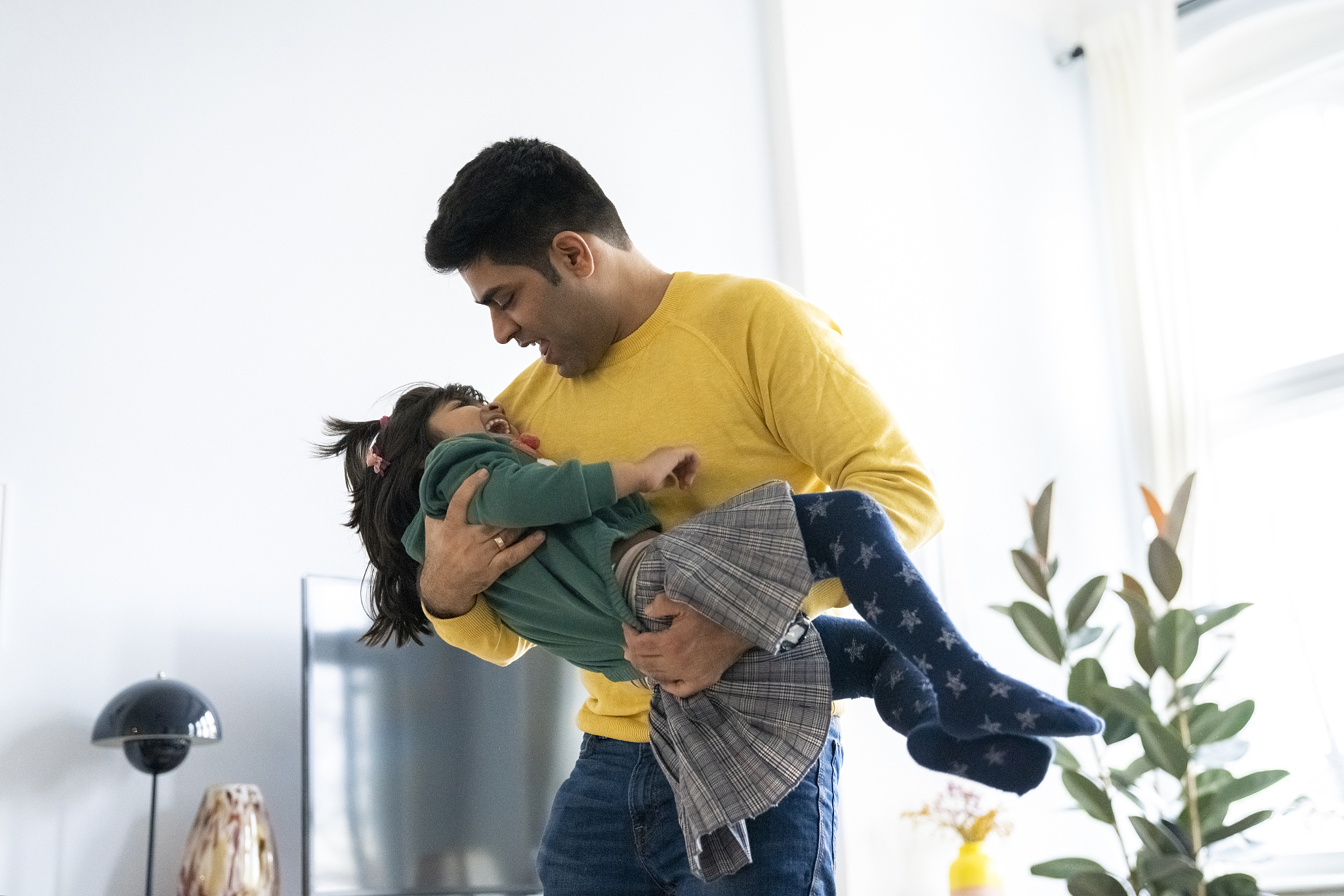 playful man carrying cute daughter in living room