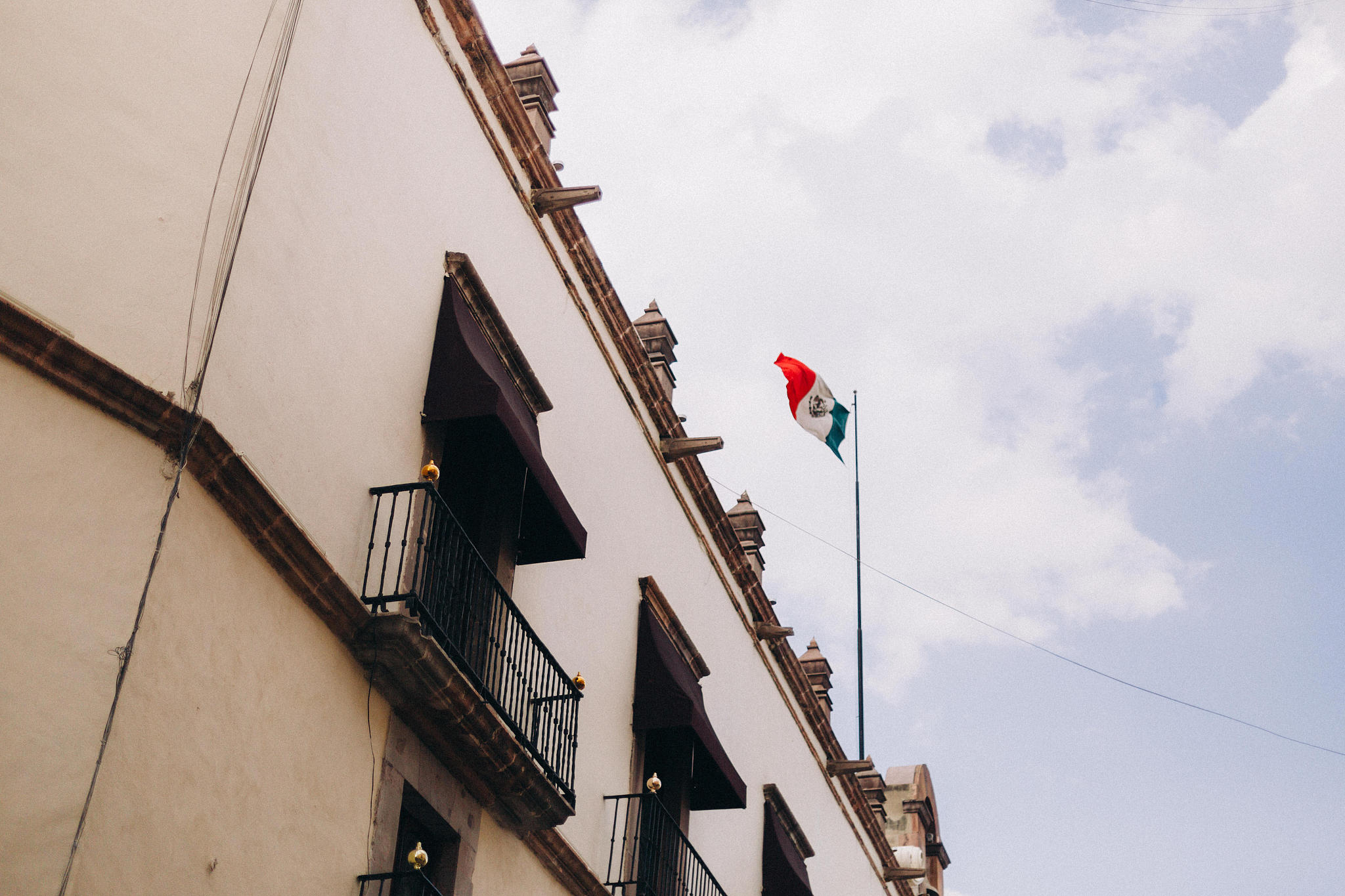 mexican flag blowing in the wind on top of a colonial building i