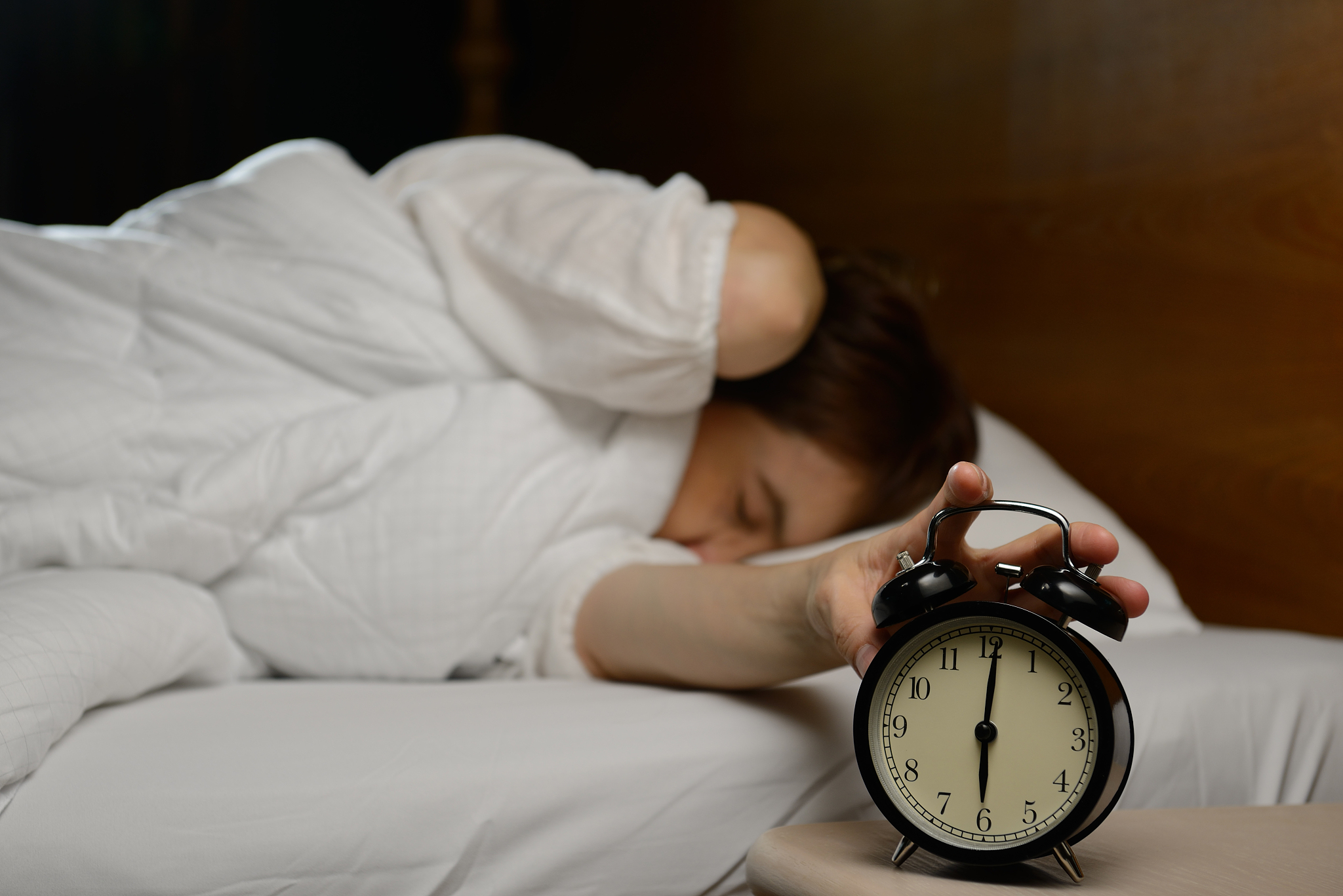 young woman turning off the alarm clock on the bed