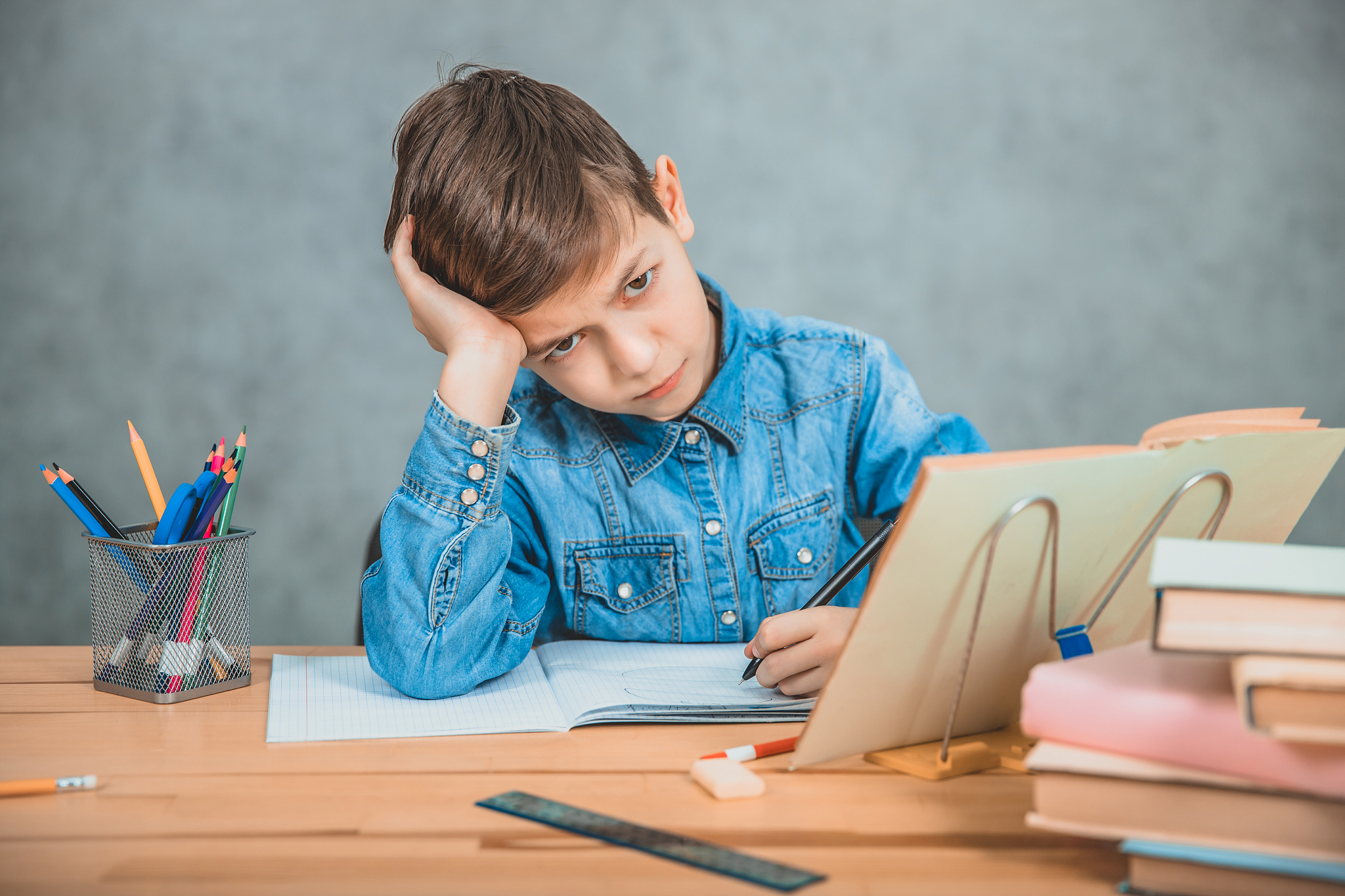 little tired schoolboy is sitting at the desk, overwhelmed with 