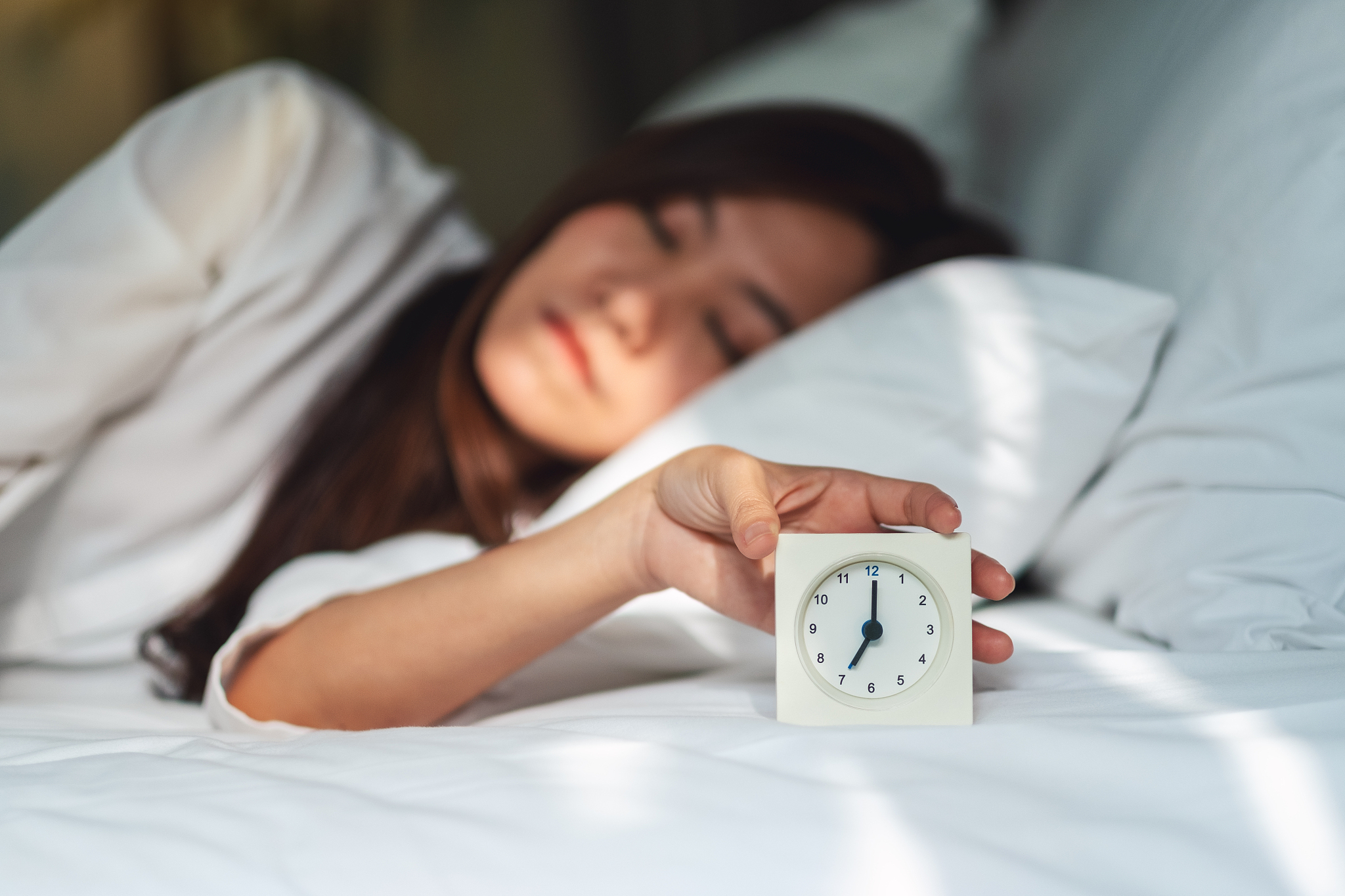 woman turning off an alarm clock while sleeping on a white cozy 