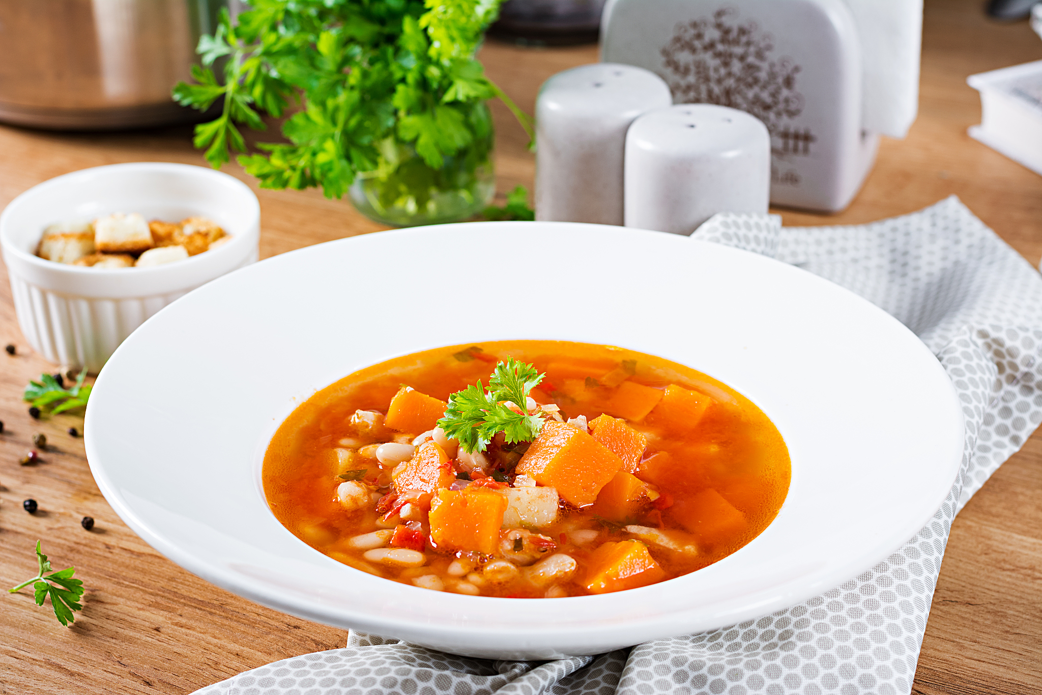 tomato chicken soup with pumpkin and white beans in white bowl.
