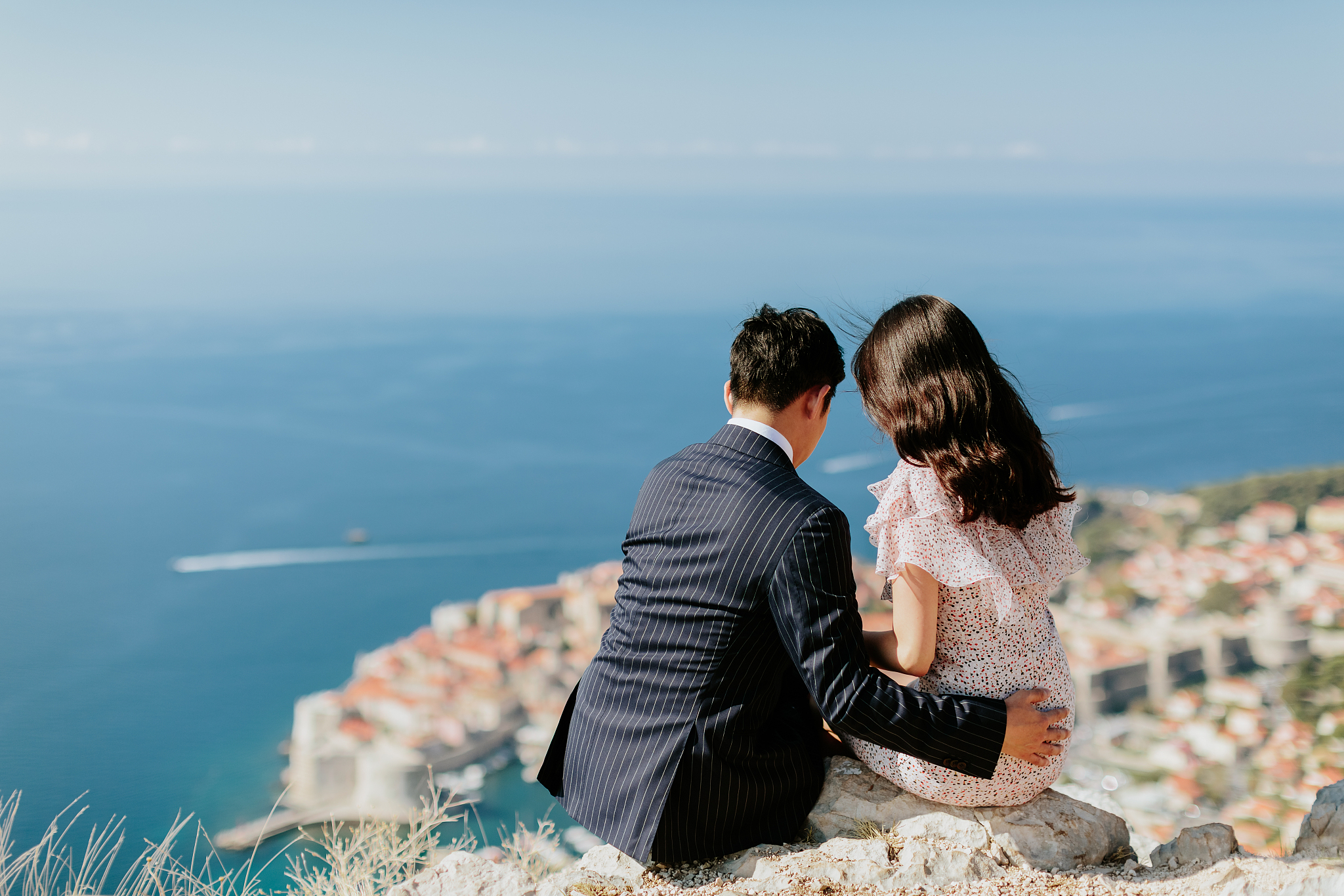 rear view of married couple sitting on rock against sea