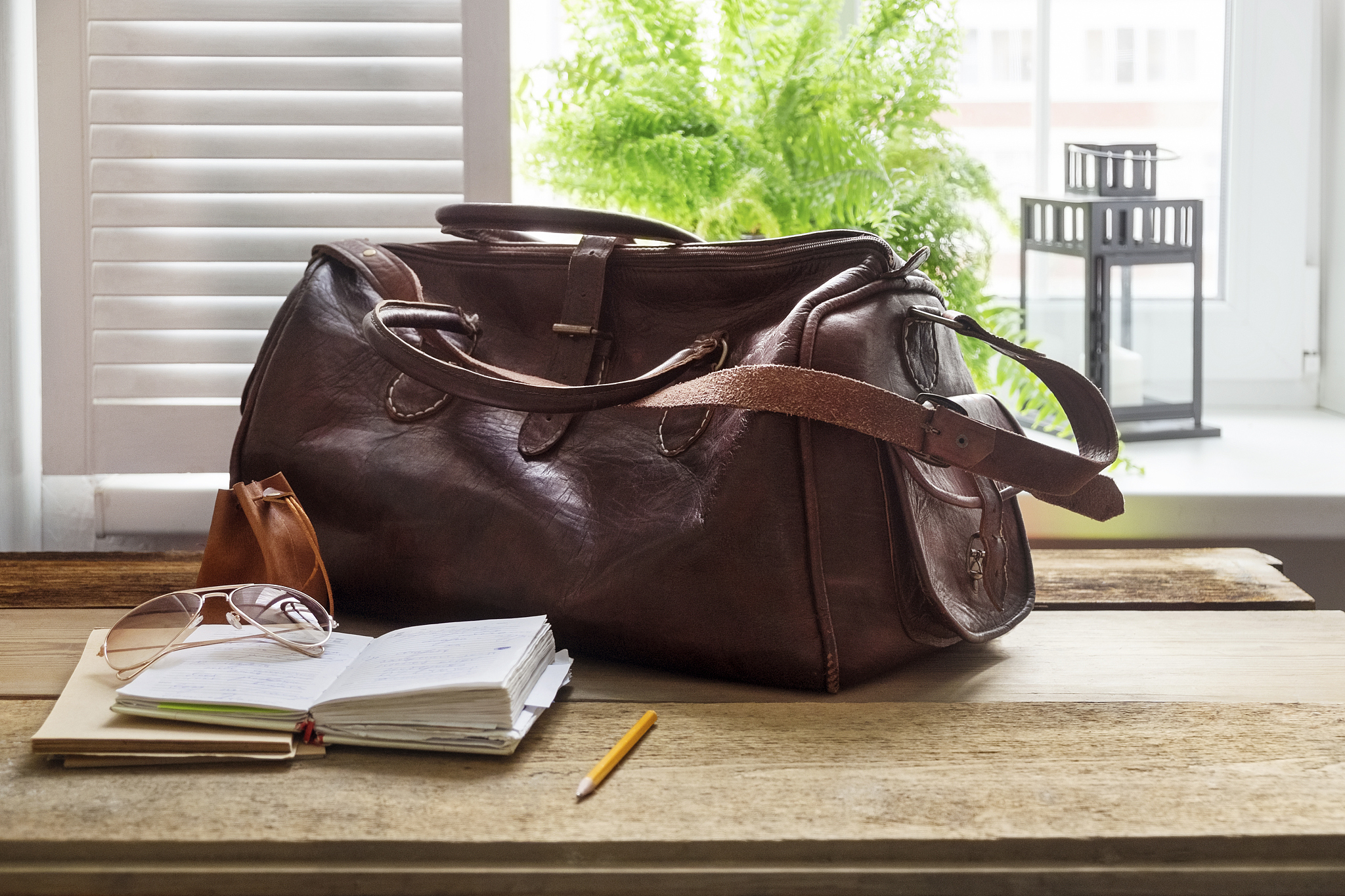 leather bag and books on table at home office by window