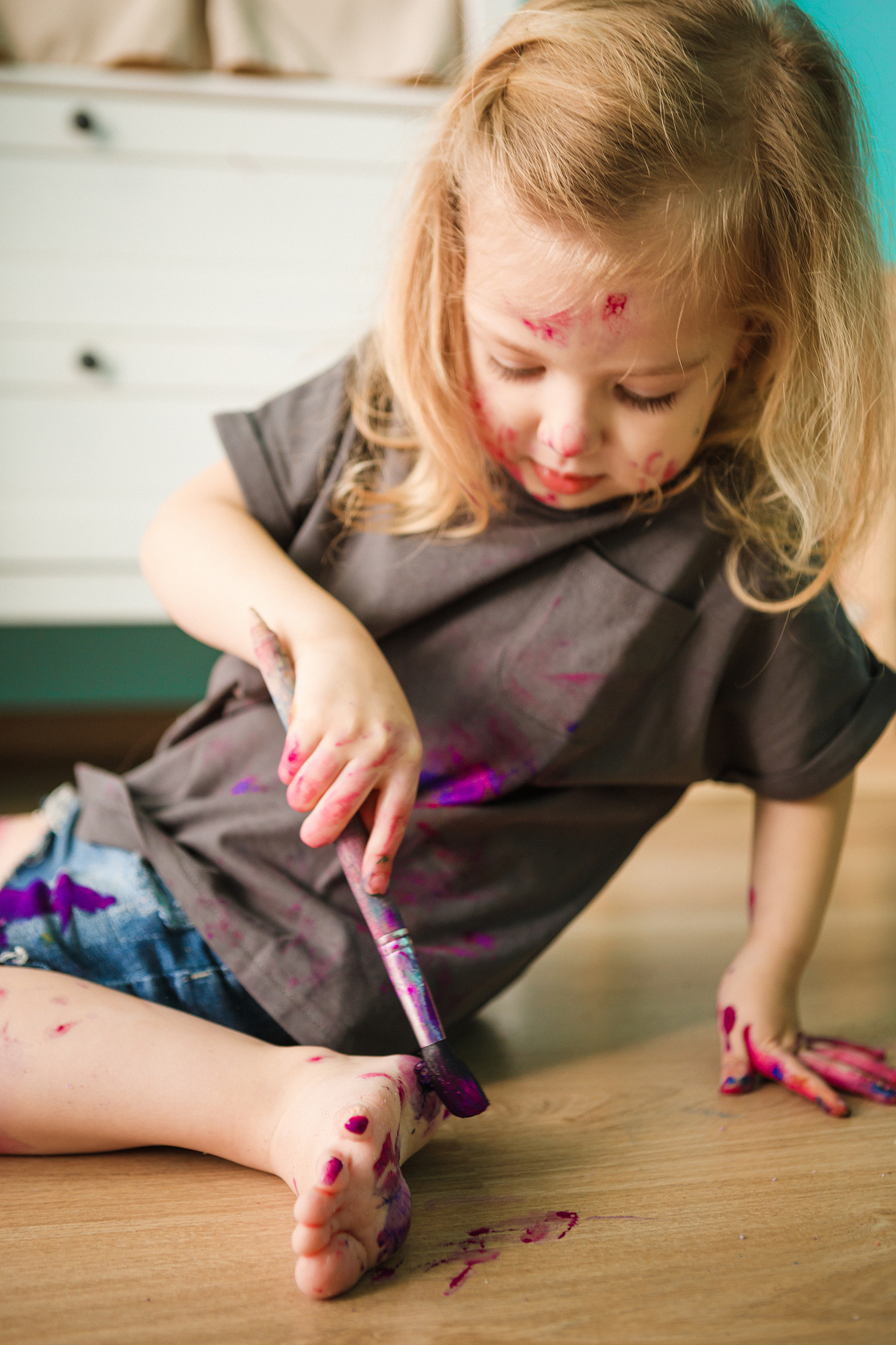 a child draws on an easel with paints while sitting on the floor