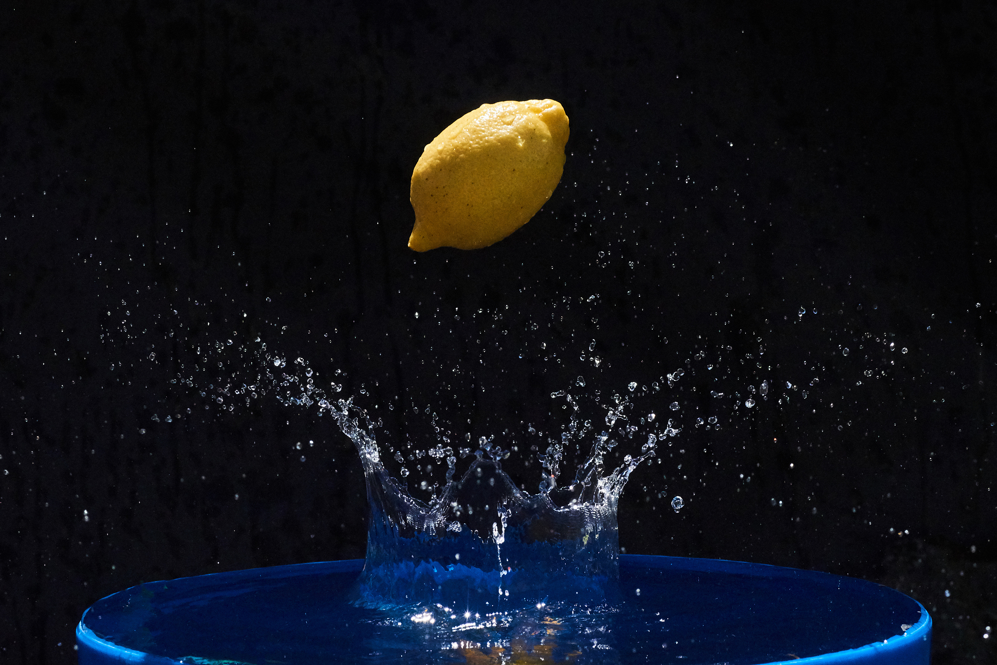 juicy yellow lemon falls in water on a black background