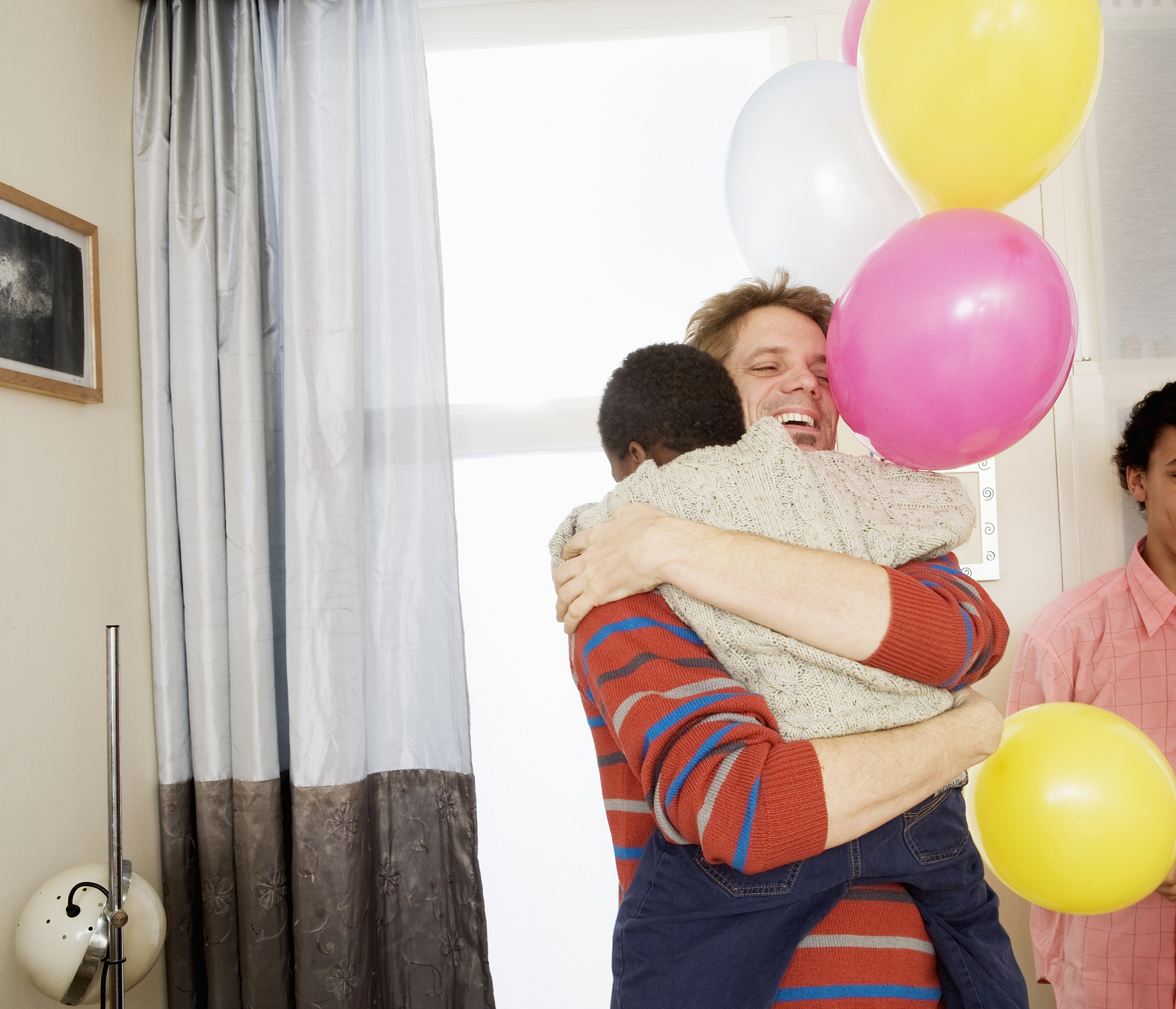 father embracing child holding balloons.
