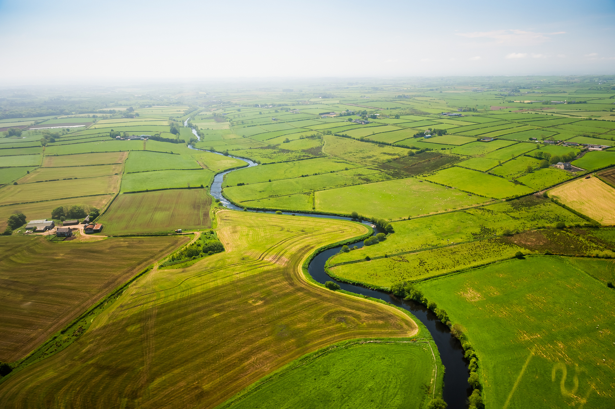 aerial view of the river flow through cultivated land and meadow
