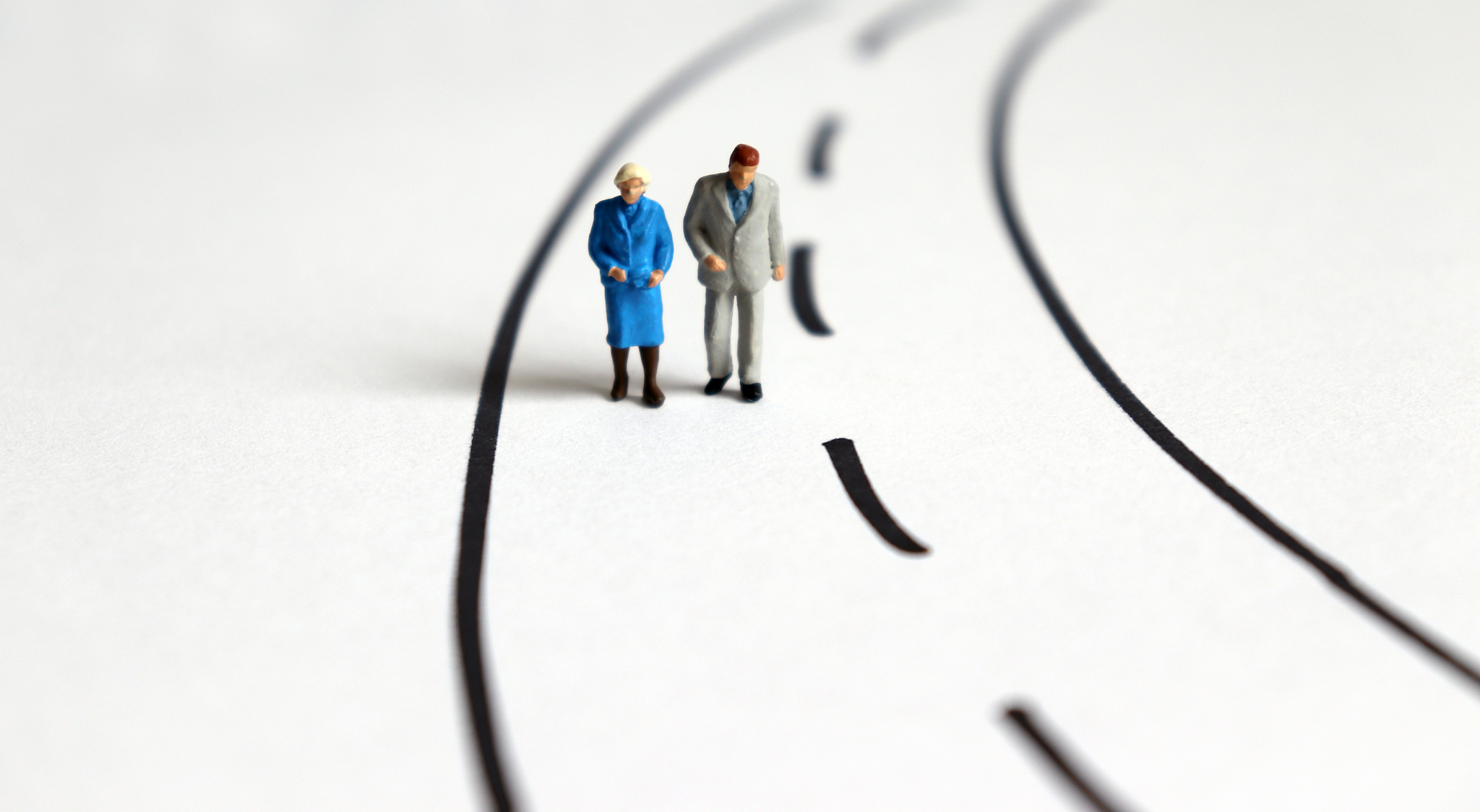 miniature old people walking  on a two lane road.