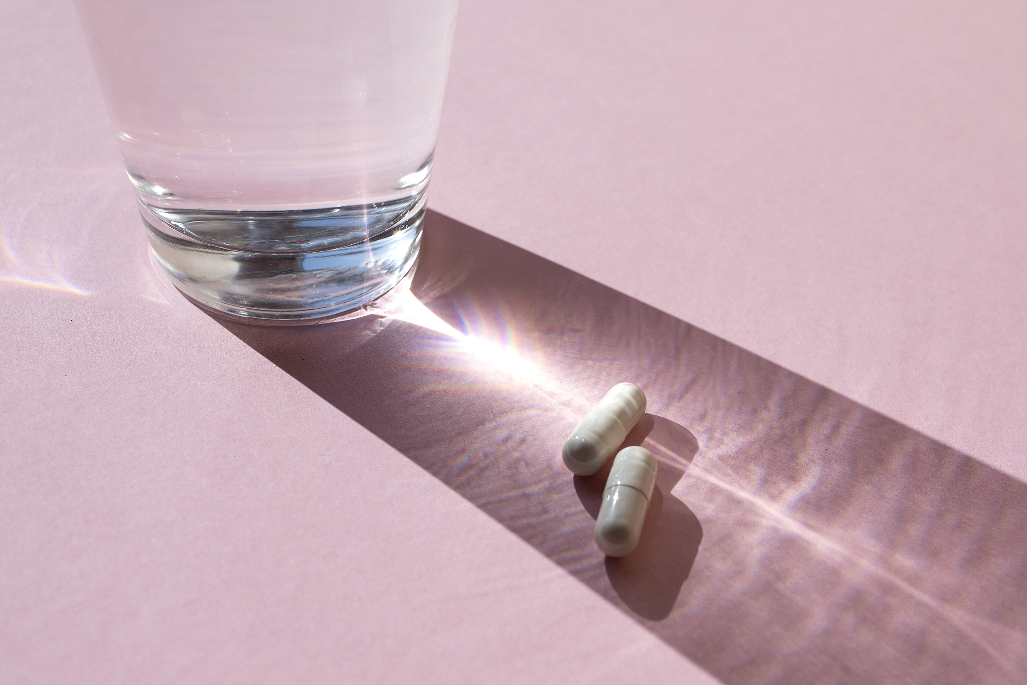 glass with pills on the pink background