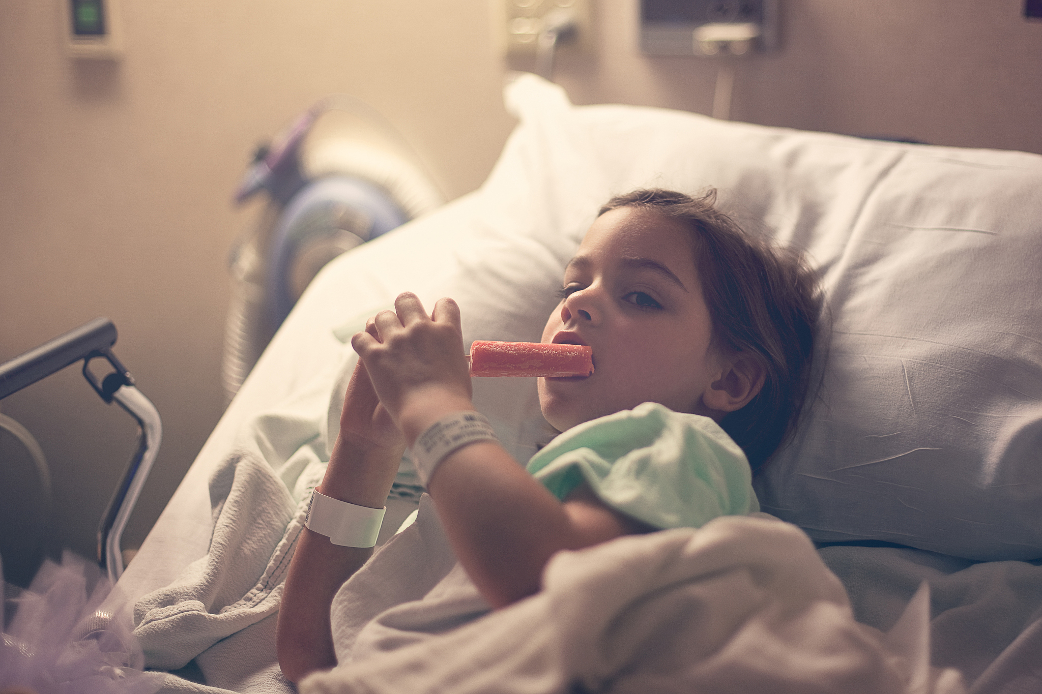 little girl in hospital bed eating popsicle