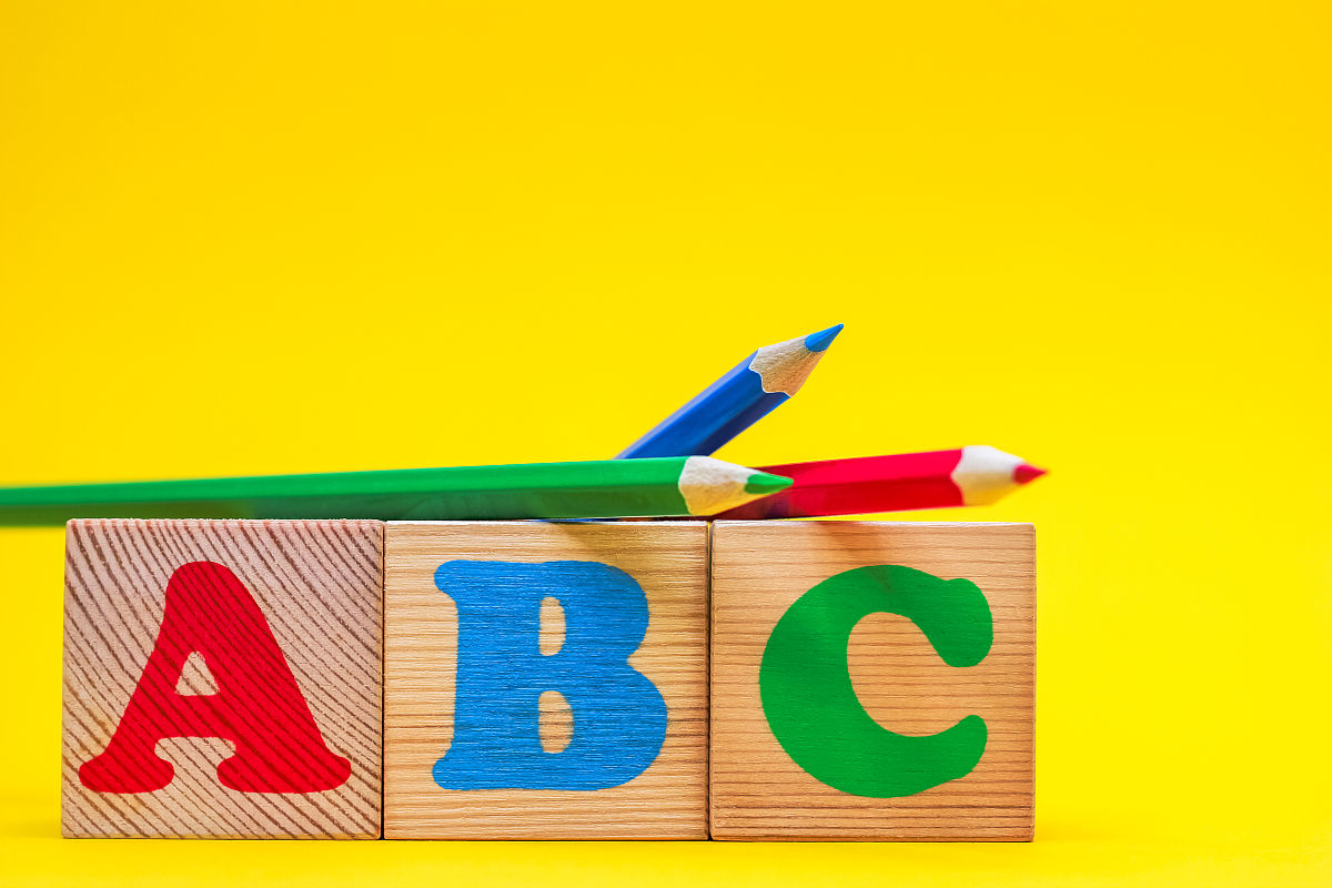 abc——英文字母的第一个字母,在黄色背景的木制玩具立方体上,旁边是