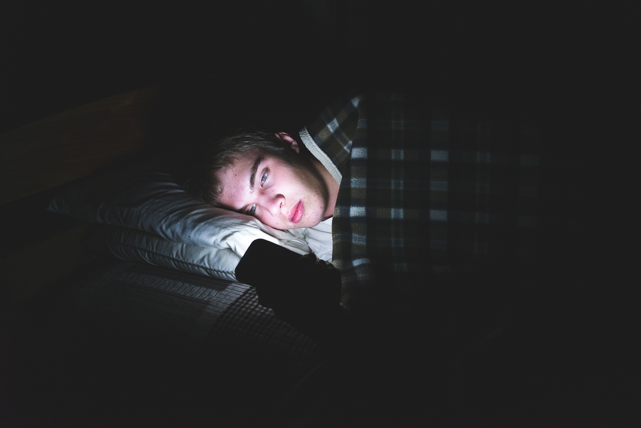 depressed teenager on his phone in the dark.