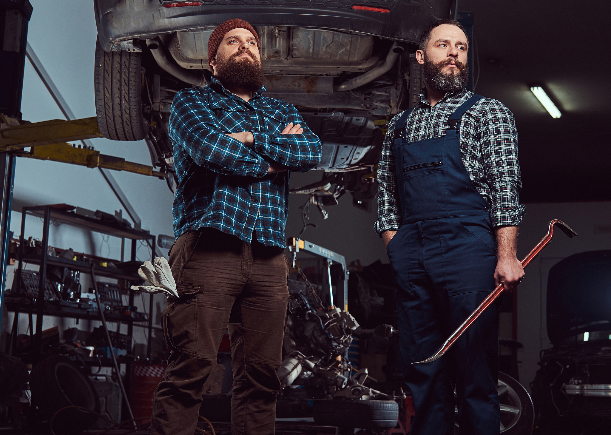 two bearded brutal mechanics repair a car on a lift in the garag