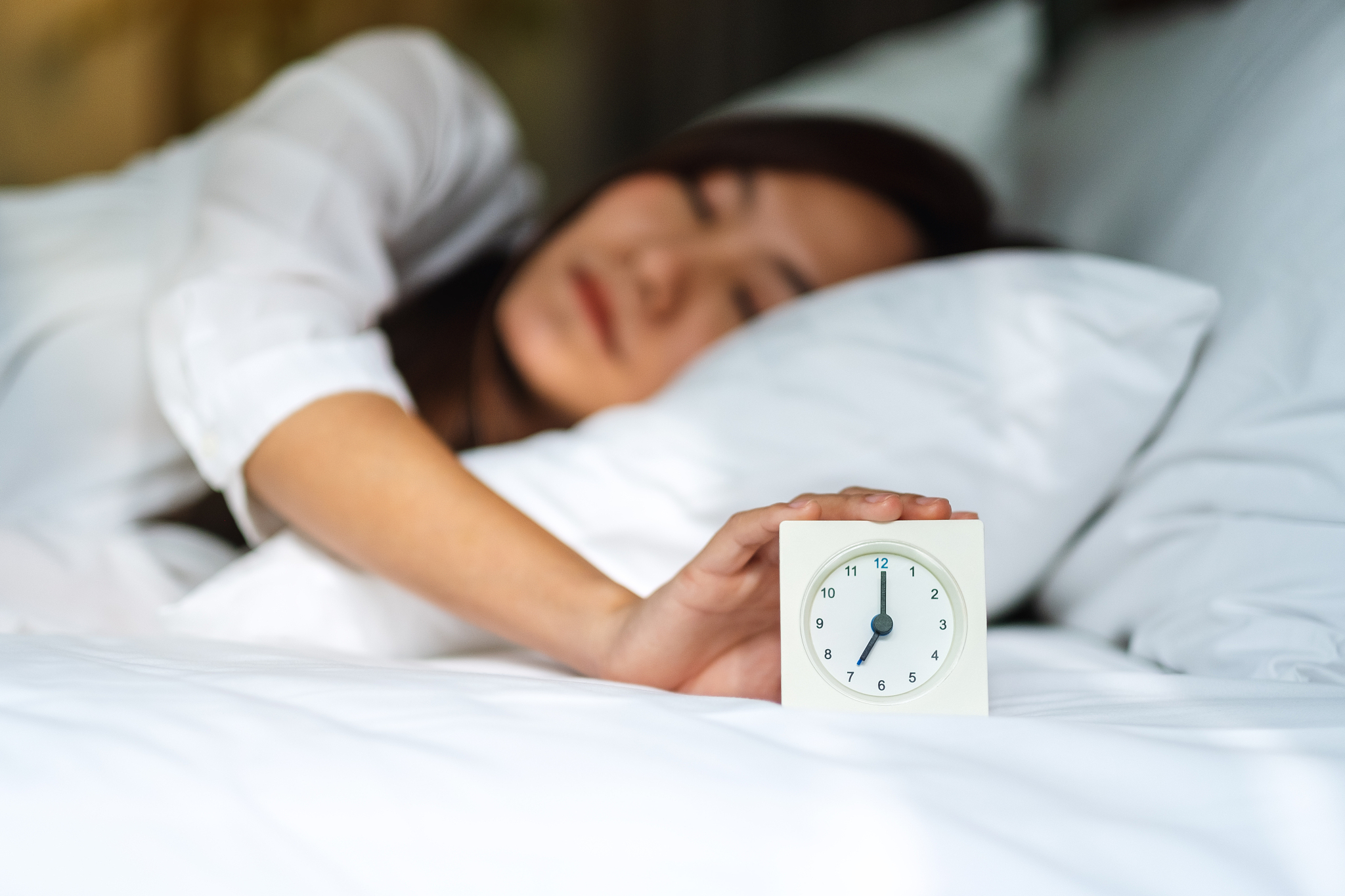 woman turning off an alarm clock while sleeping on a white cozy 
