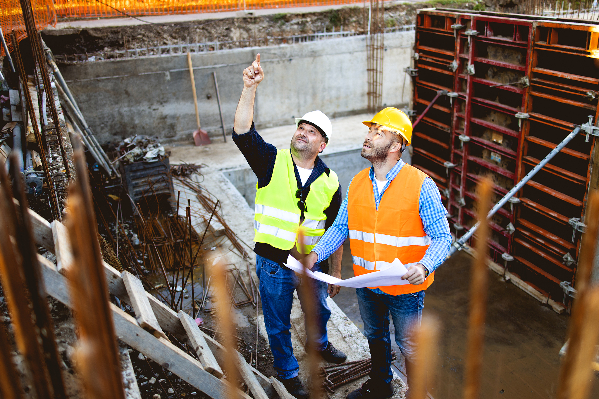men in hardhat and yellow and orange jacket posing on building s