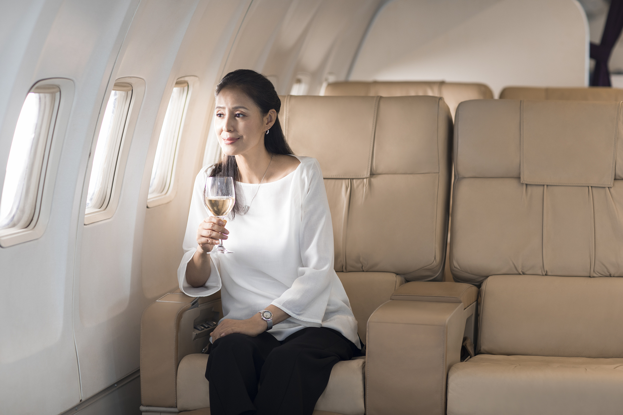 优雅的中年女士在机舱里喝葡萄酒