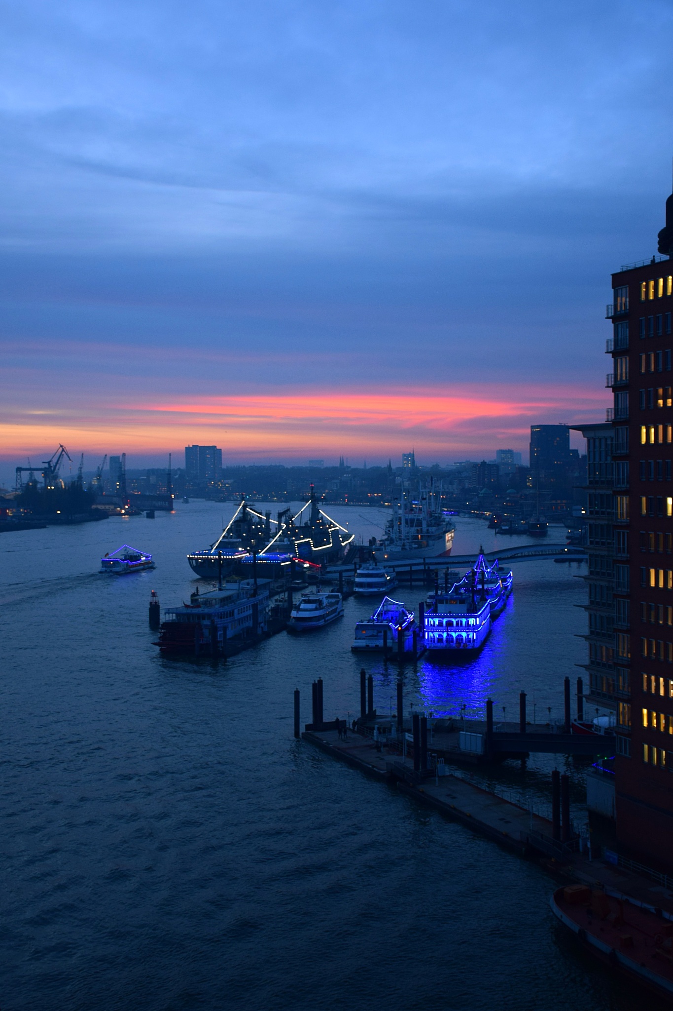 illuminated city by sea against sky at sunset