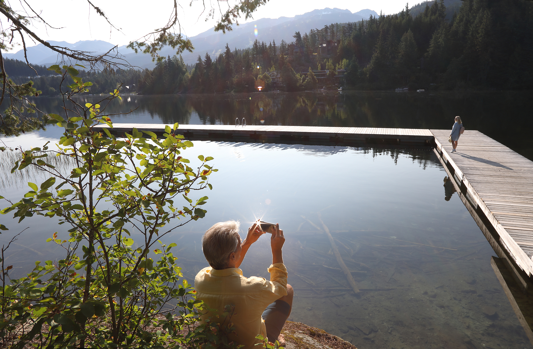 man relaxes on bluff above lake, takes smart phone pic